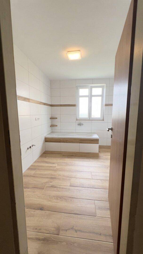 Badezimmer mit Holzbodenfliesen, weiß gefliesten Wänden und Badewanne.