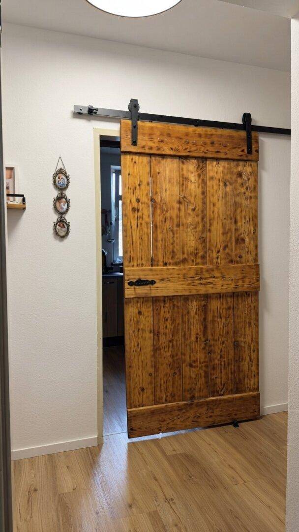 Rustikale Schiebetür aus Holz, die den Wohnbereich von der Küche trennt.