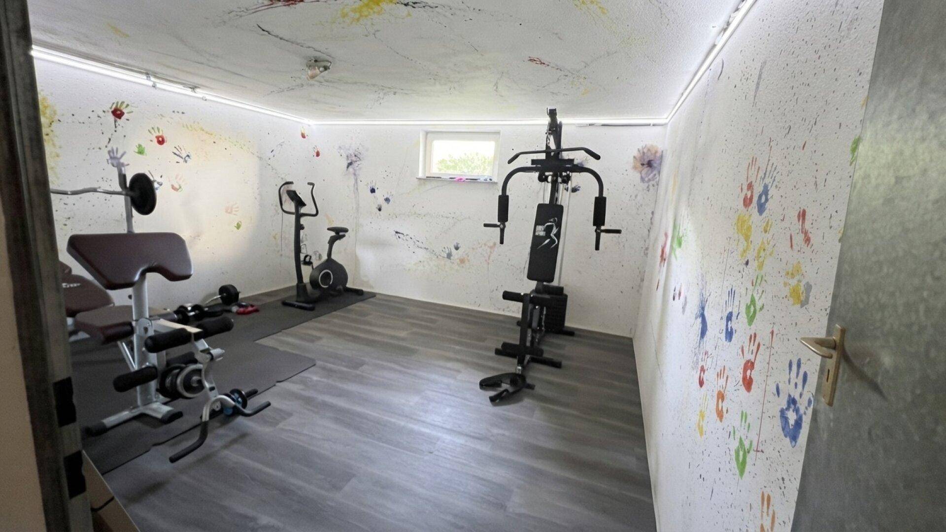 Fitnessraum im Keller mit verschiedenen Trainingsgeräten und farbenfrohen Wänden.