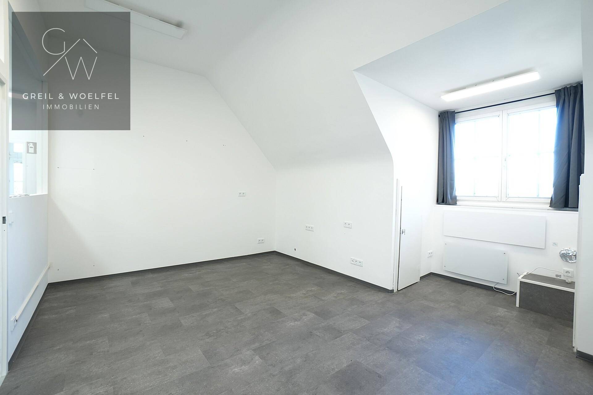Leerer Büroraum im Dachgeschoss mit Schrägdach, Fenster und Heizkörper.