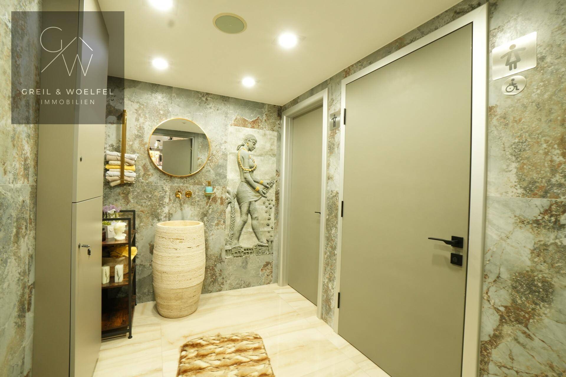 Moderne Toilette mit stilvollen Wandfliesen, runden Spiegel und barrierefreien Elementen.