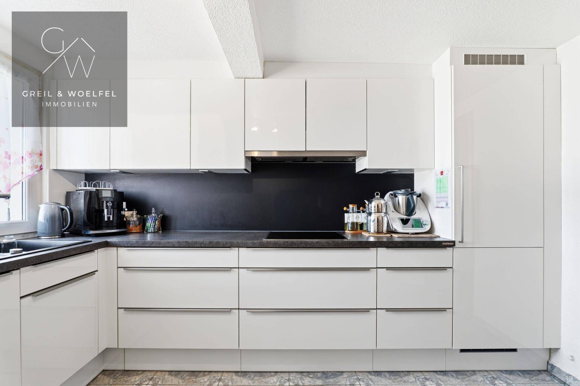 Moderne Einbauküche mit weißen Hochglanzfronten, dunkler Arbeitsplatte und integrierten Geräten.