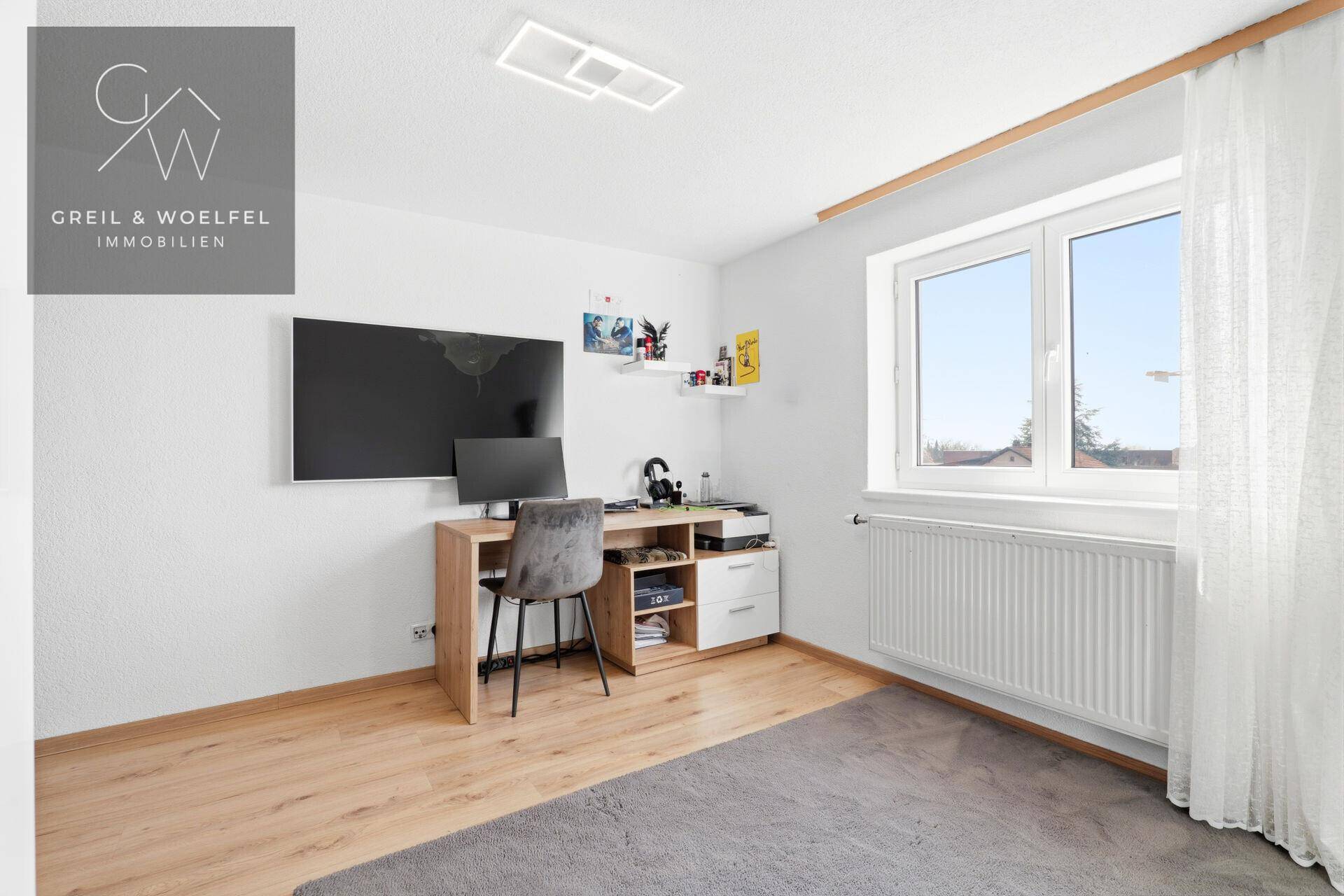 Jugendzimmer mit Schreibtisch, großem Fernseher und hellem Fenster, perfekt für Arbeit und Freizeit.