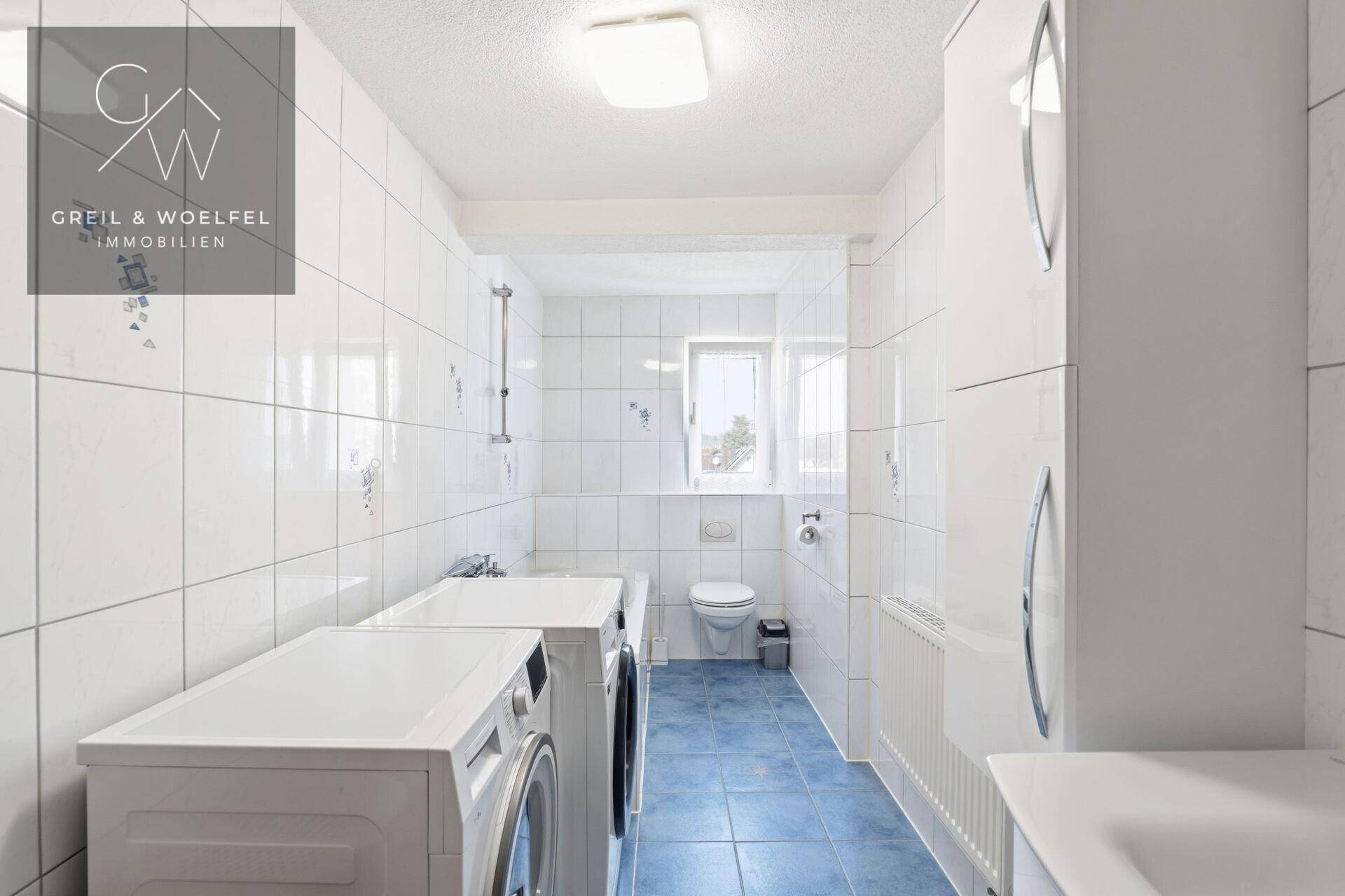 Funktionales Badezimmer mit Toilette, Waschmaschinen und weißen Fliesen, bietet ausreichend Platz.