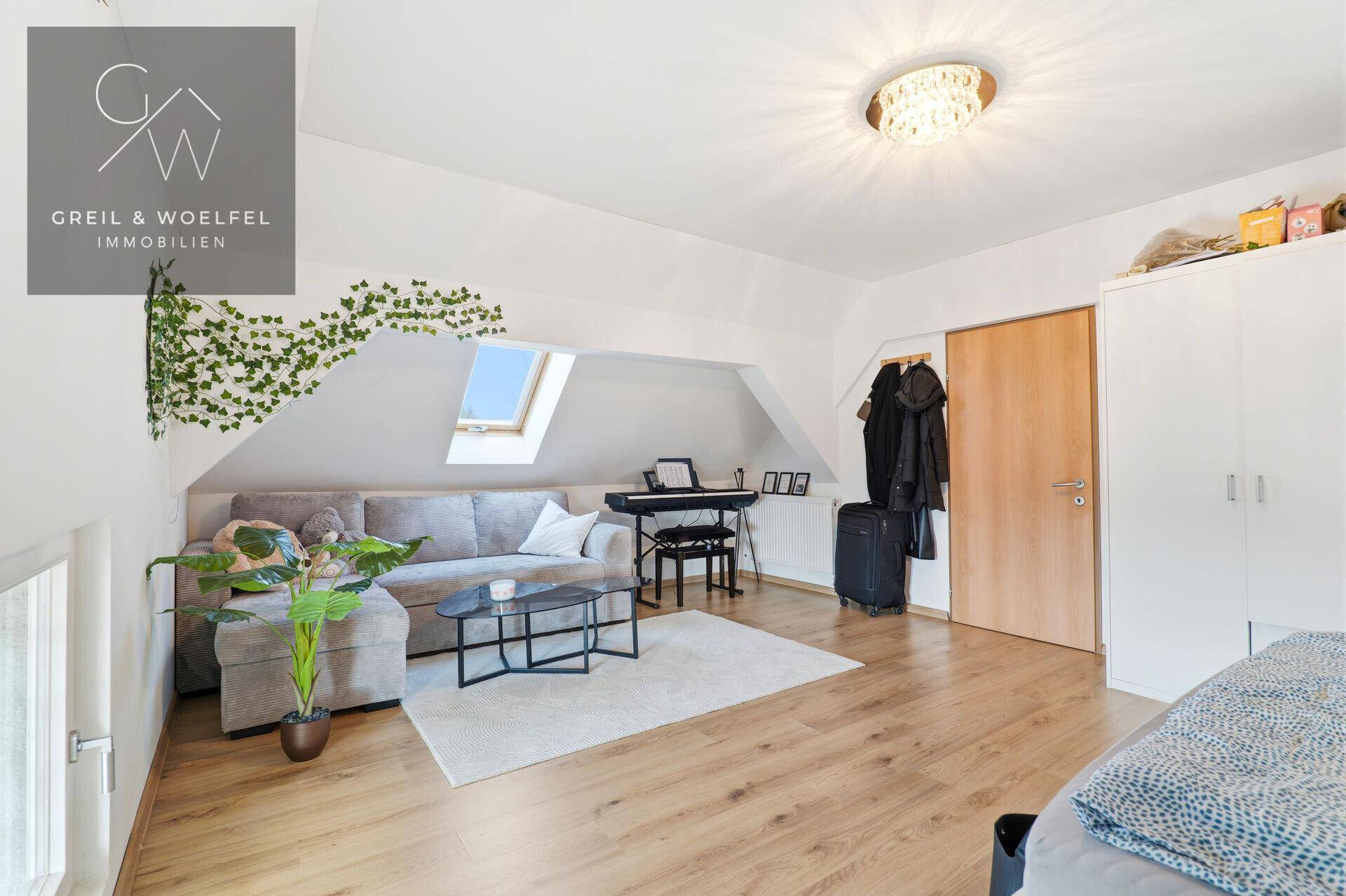 Geräumiges Dachzimmer mit Sofa, Keyboard, Kleiderschrank und Dachfenster, ideal für Hobbys und Entspannung.