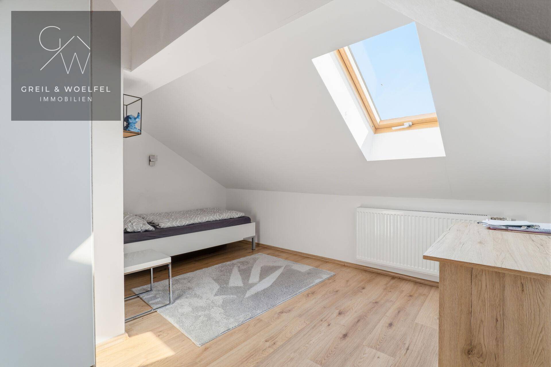 Helles Dachzimmer mit Einzelbett, Schreibtisch und großem Dachfenster, ideal als Kinder- oder Gästezimmer.