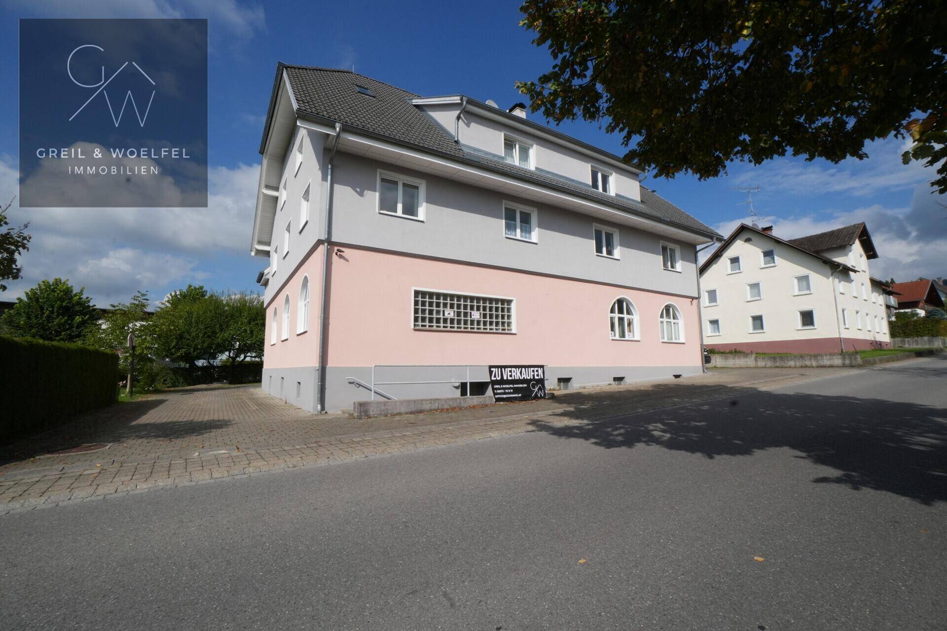 Mehrstöckiges Wohngebäude mit rosa und grauer Fassade an einer ruhigen Straße gelegen.