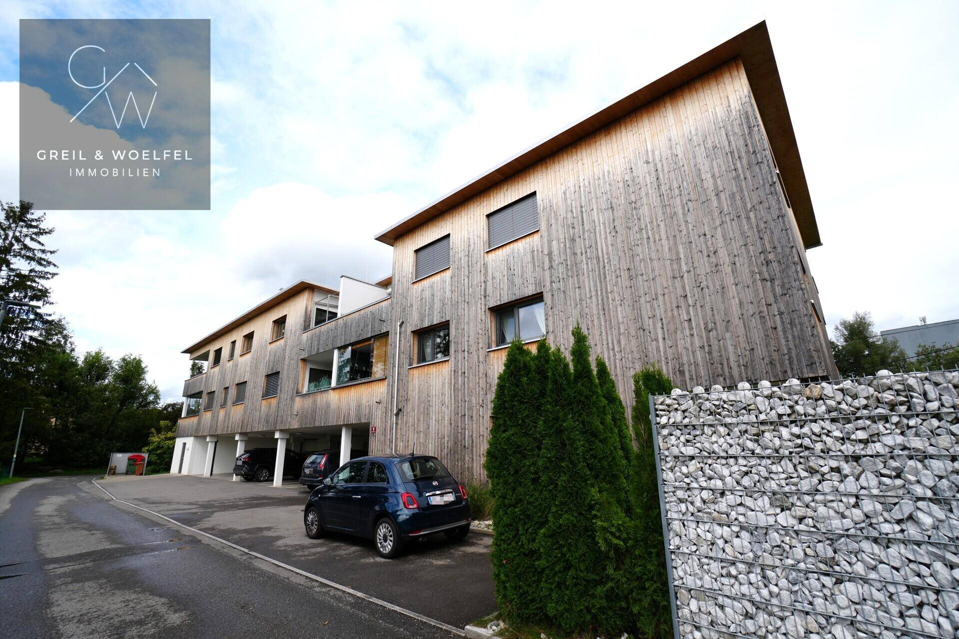 Modernes Mehrfamilienhaus mit Holzfassade und integrierten Balkonen in grüner Umgebung.