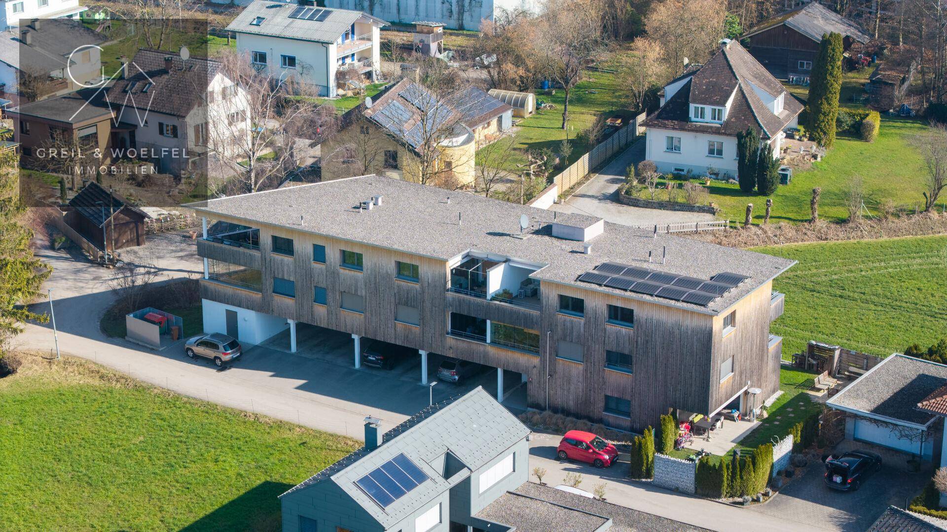 Luftaufnahme des modernen Wohngebäudes mit Holzfassade und Photovoltaikanlage auf dem Dach.