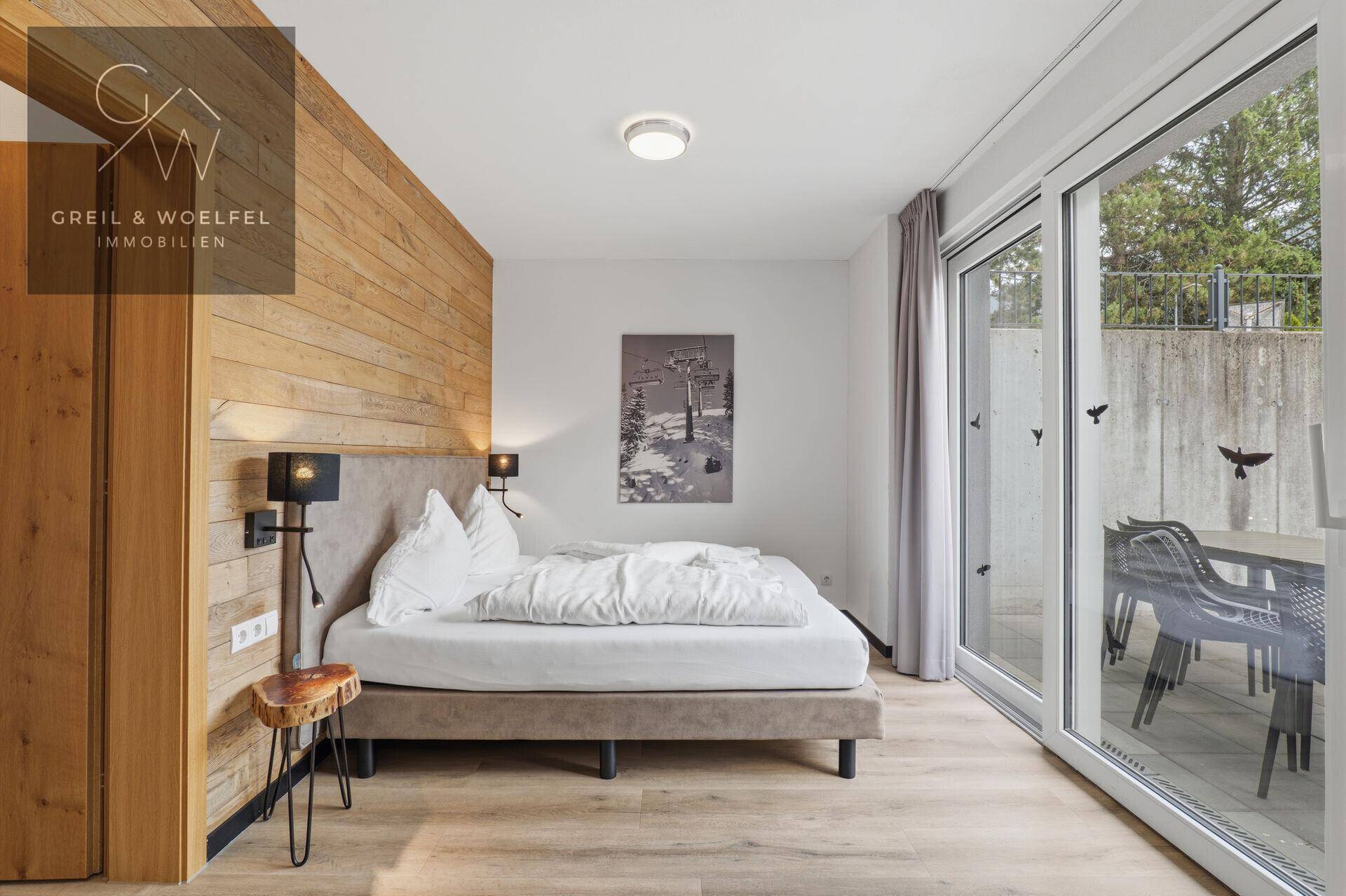 Helles Schlafzimmer mit Holzwand, Doppelbett und direktem Zugang zur Außenterrasse.