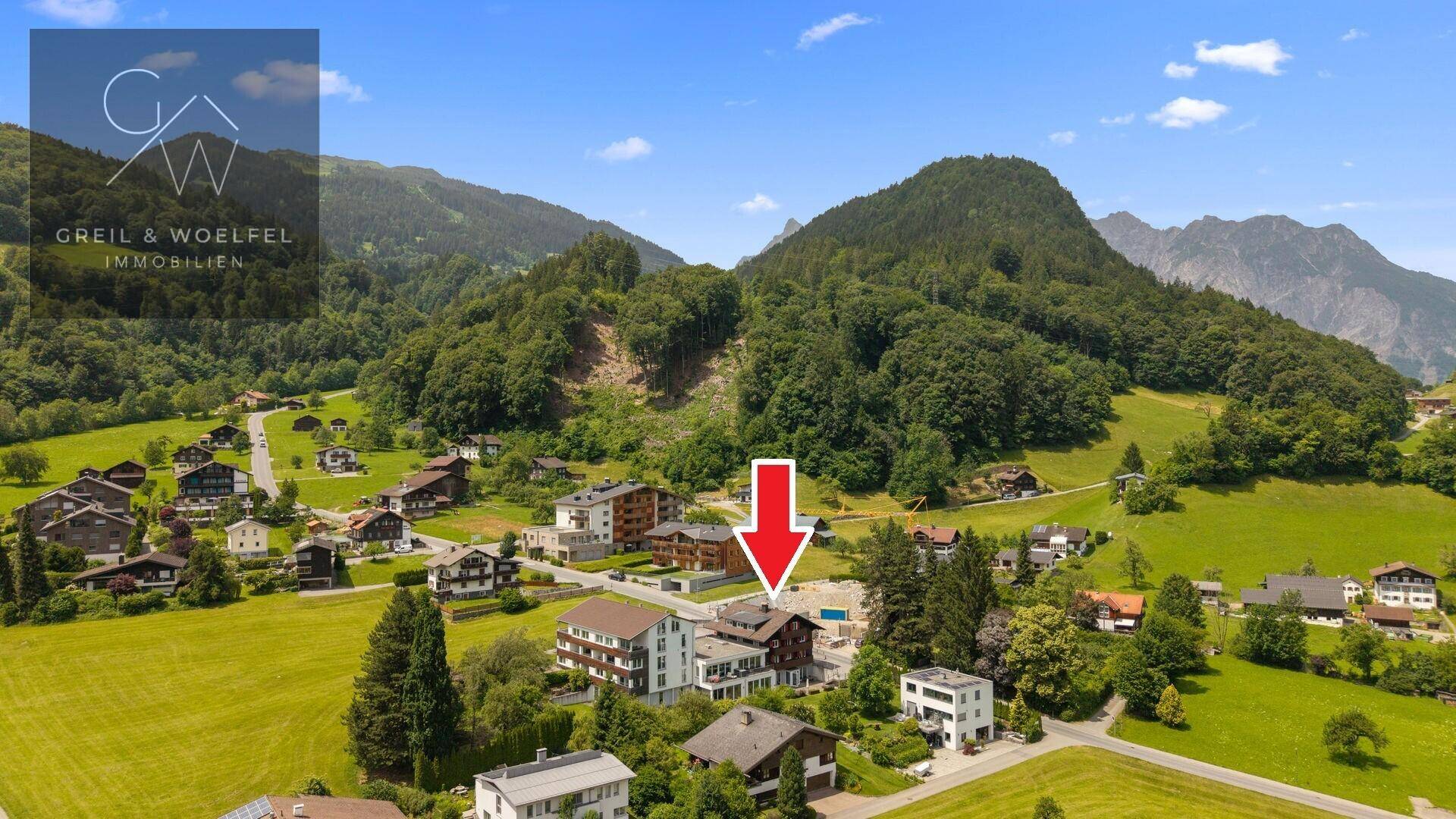 Luftaufnahme eines Anwesens in einer grünen Berglandschaft mit umliegenden Häusern.