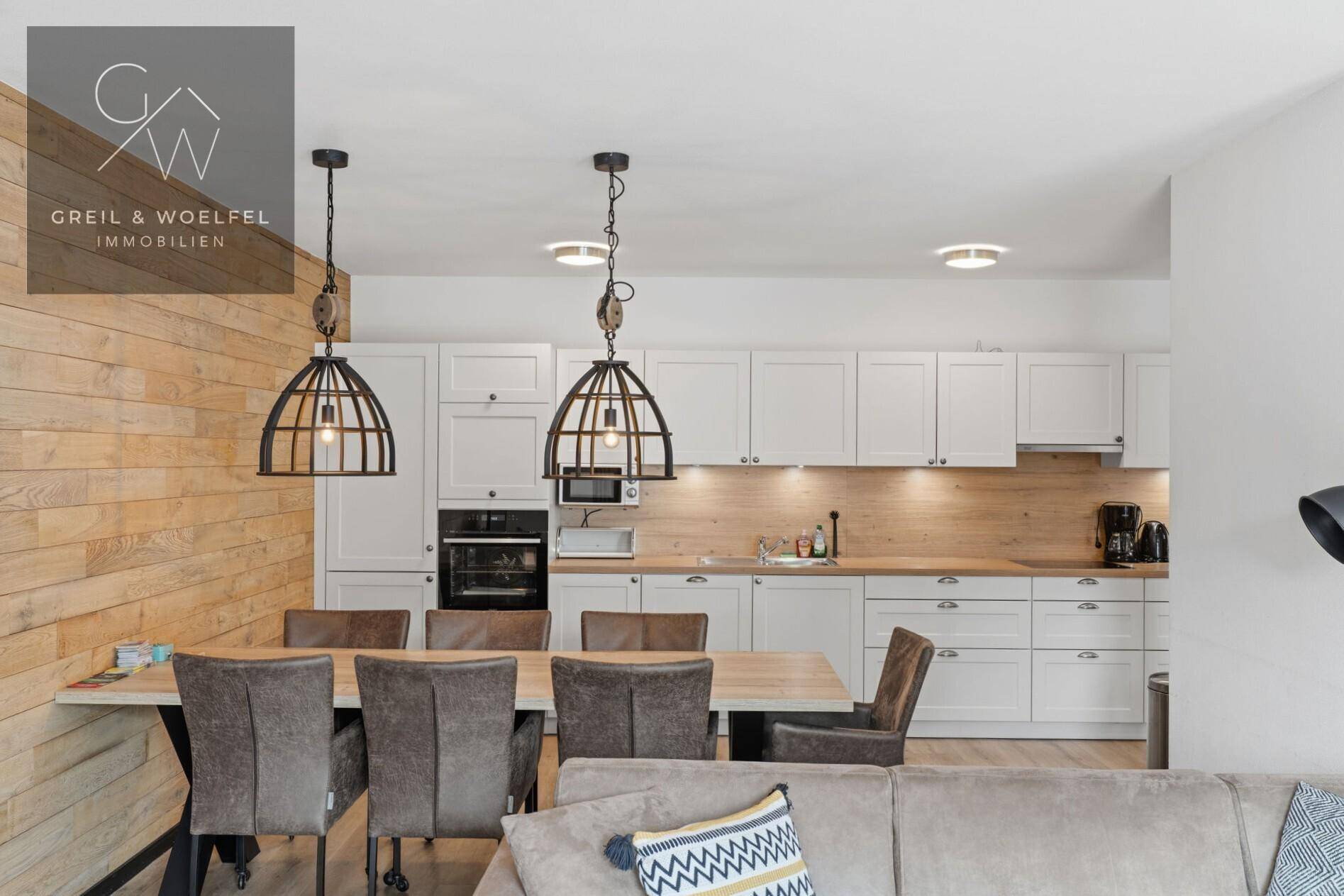 Moderne Einbauküche mit weißen Schränken, Holzarbeitsplatte und großem Esstisch.