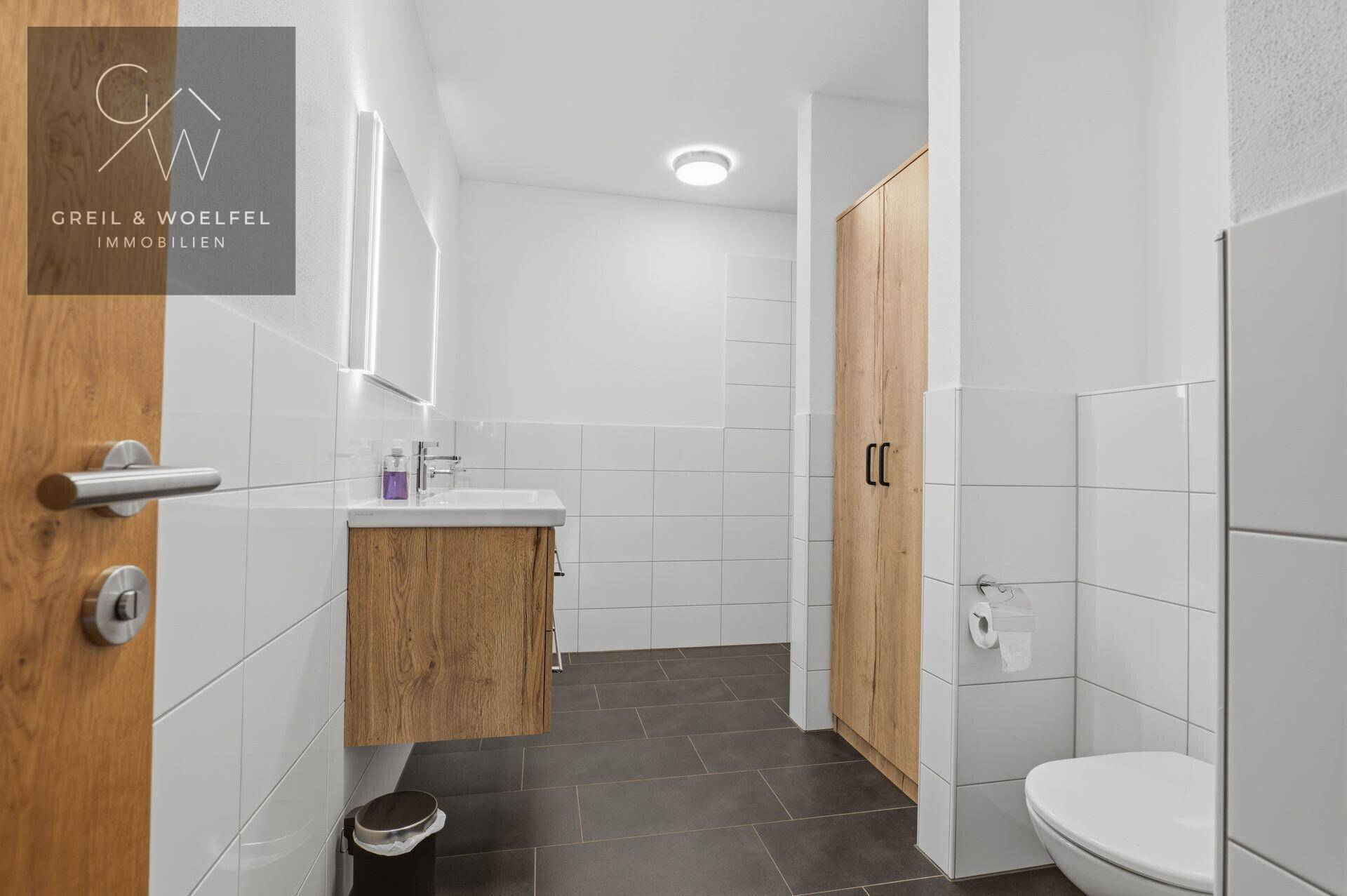Helles Badezimmer mit modernem Waschtisch, Toilette und integriertem Spiegelschrank.