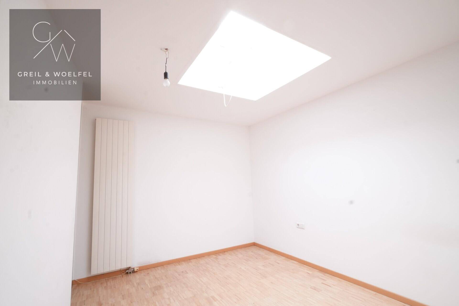Heller Raum mit Parkettboden, Heizkörper und einem großen Dachfenster für viel Tageslicht.