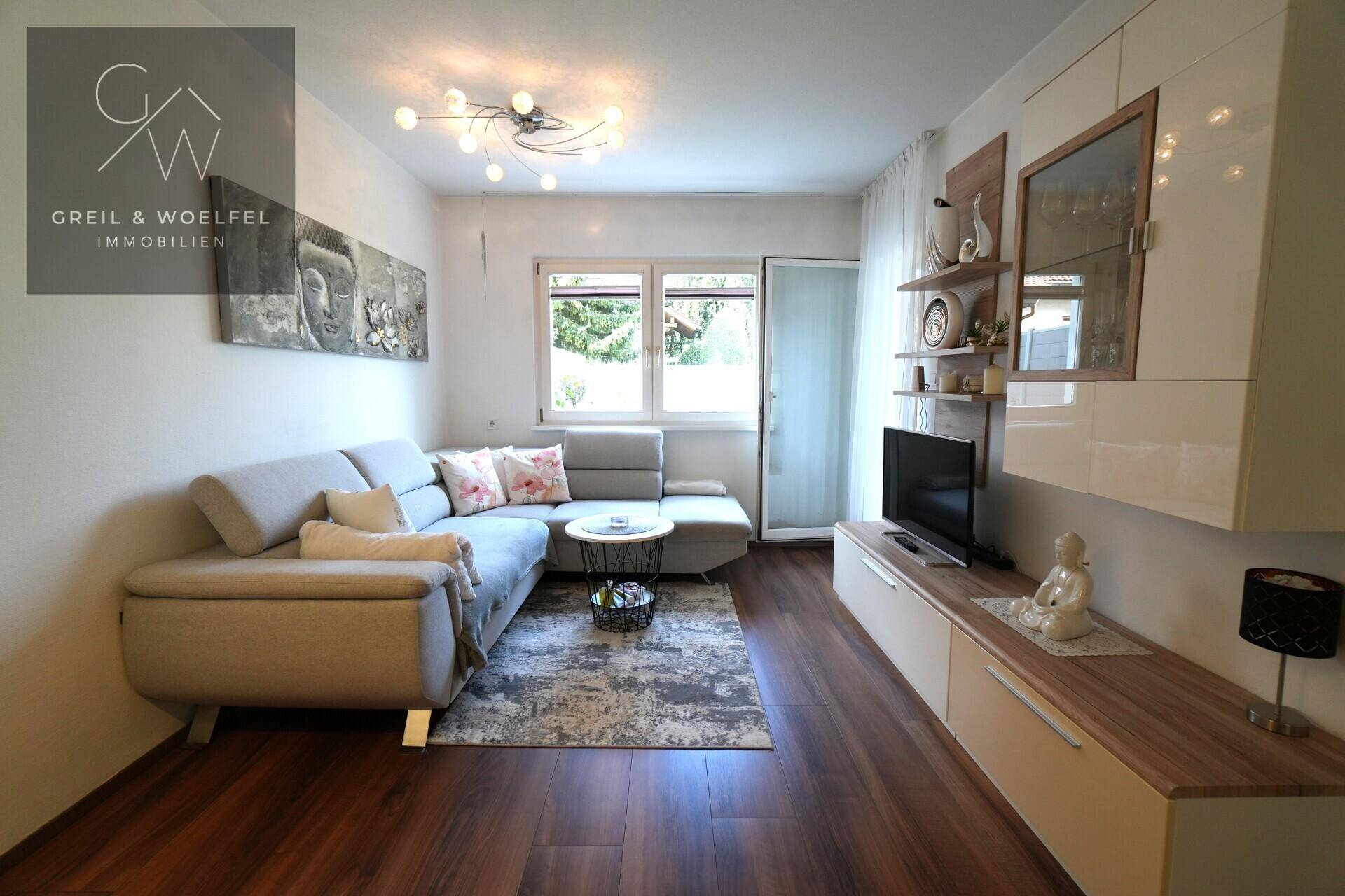 Gemütliches Wohnzimmer mit dunklem Holzboden, Ecksofa und Zugang zu einem Außenbereich.