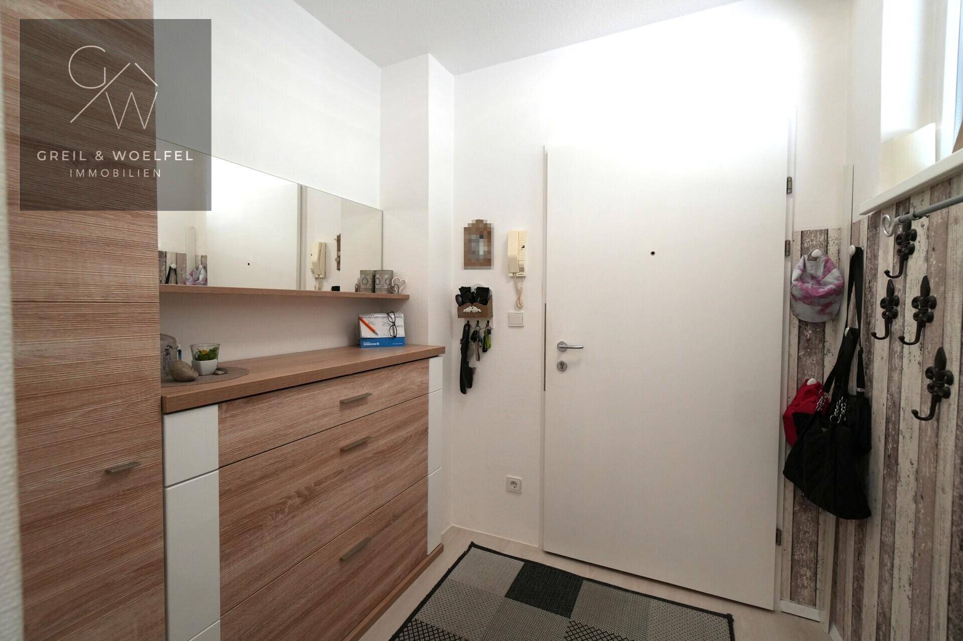 Eingangsbereich mit Holzschuhschrank, Spiegel und Garderobenhaken für Kleidung.