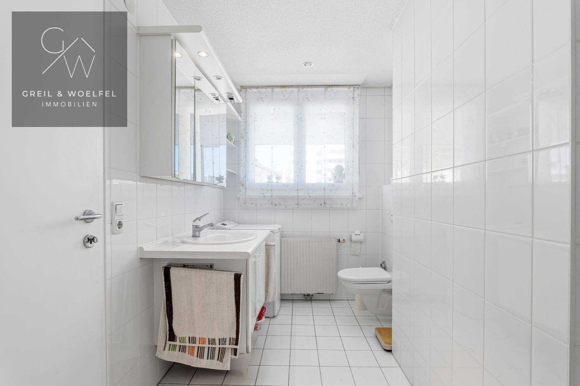 Modern gefliestes Badezimmer mit Waschbecken, Toilette und Spiegelschrank.