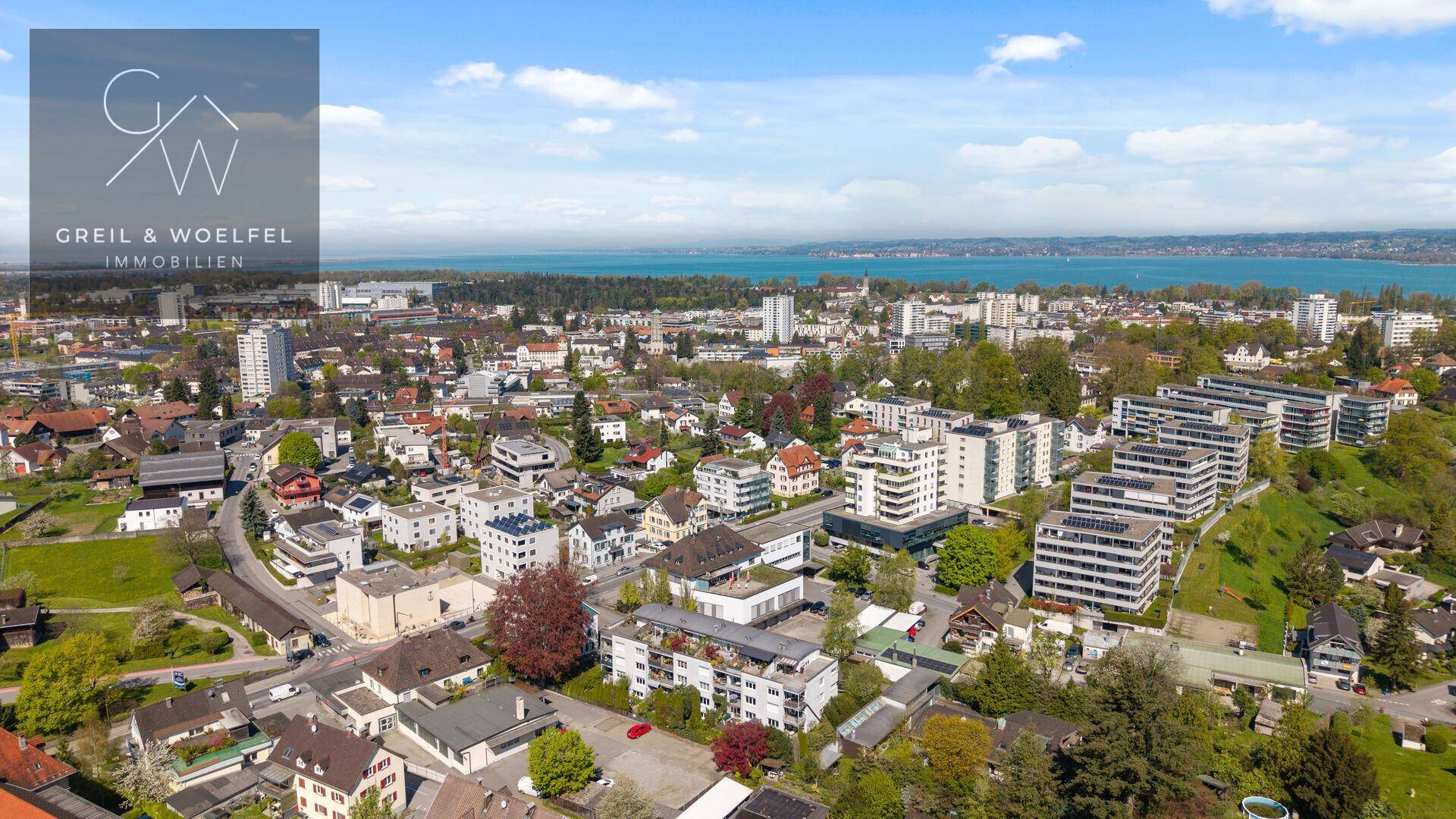 Panoramablick auf eine Stadt am See mit weitläufiger Bebauung und Bergen am Horizont.