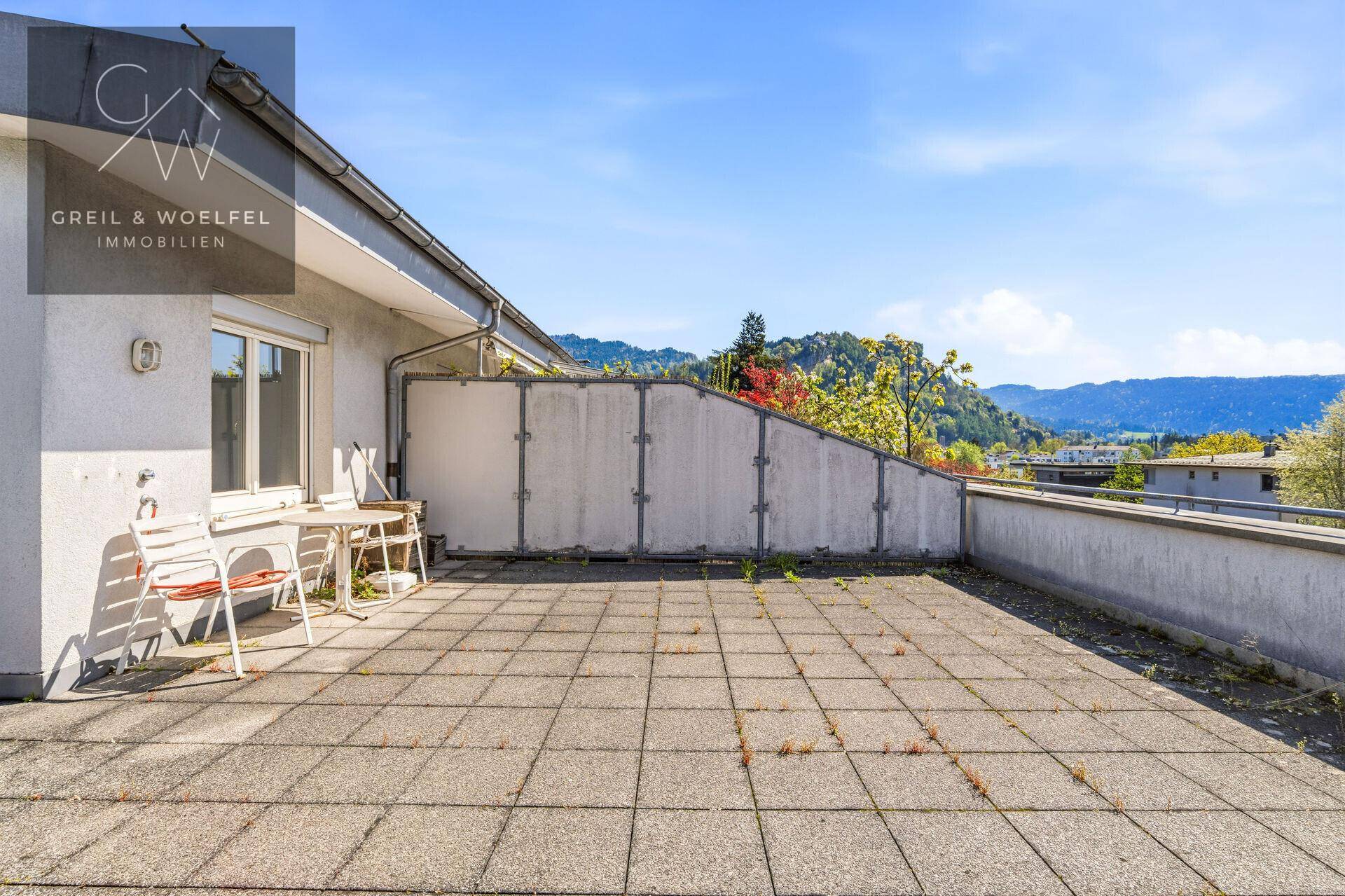 Weitläufige Dachterrasse mit Fliesenboden und Blick auf die grüne Umgebung.