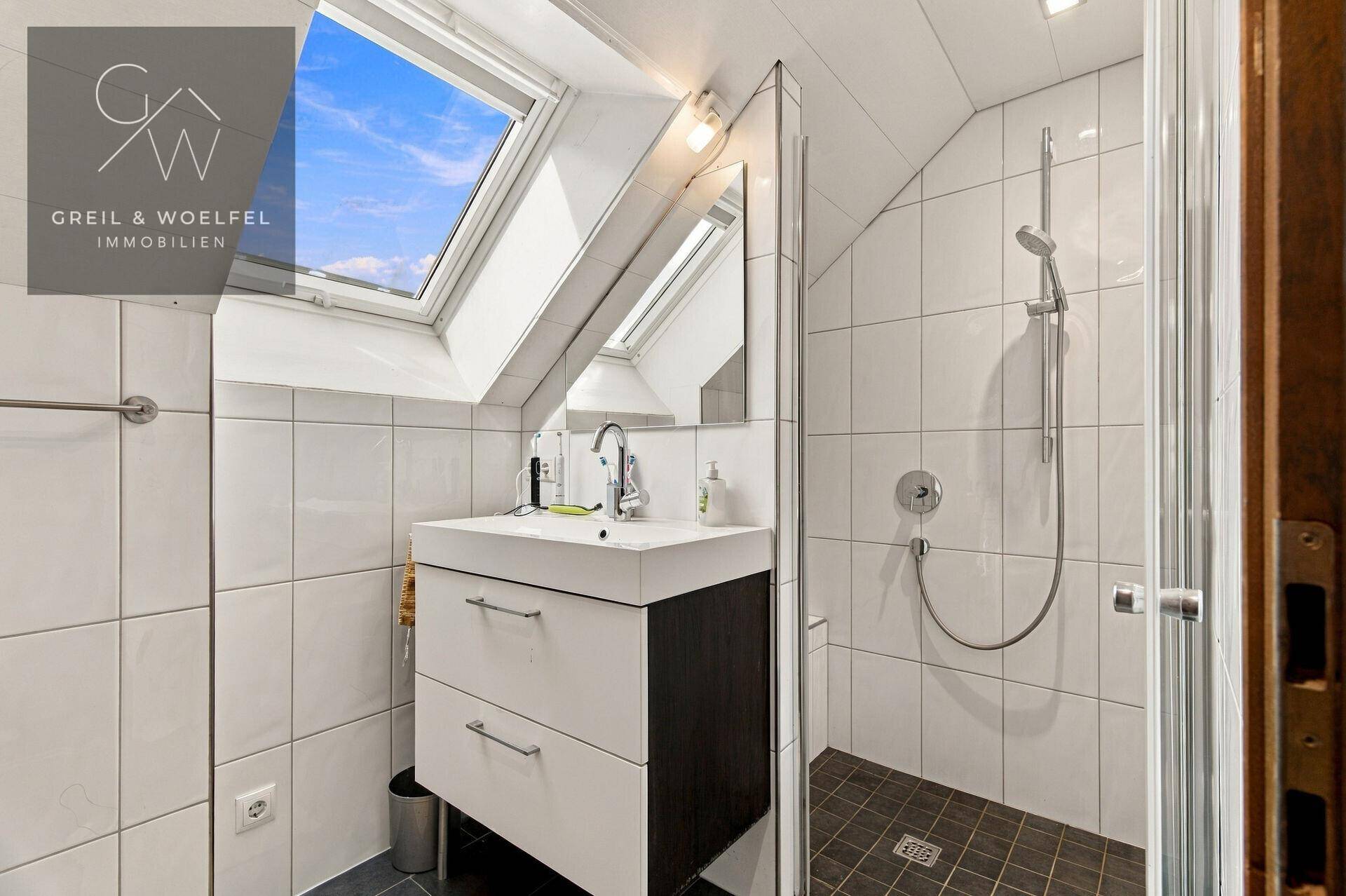 Modernes Badezimmer mit Dusche, Waschbecken und Dachfenster, hell gefliest.