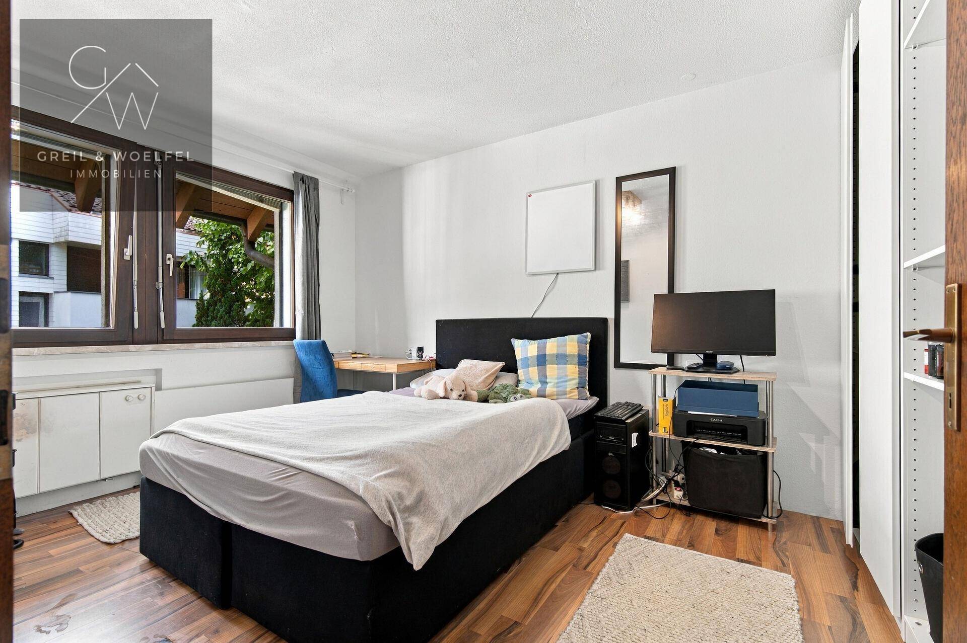 Helles Schlafzimmer mit großem Fenster, Holzboden und ausreichend Platz für Möbel.