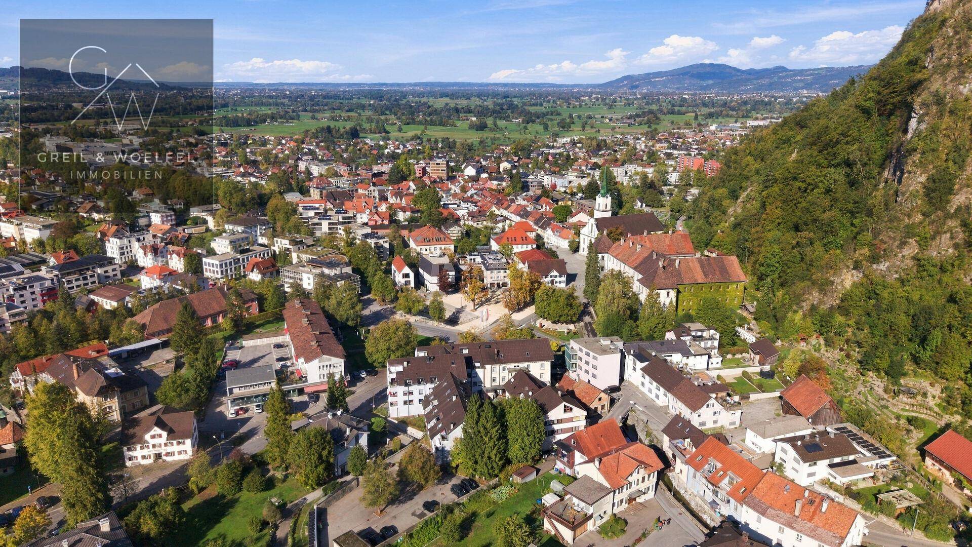 Weitläufige Luftaufnahme einer Siedlung mit grüner Umgebung und Bergen im Hintergrund.
