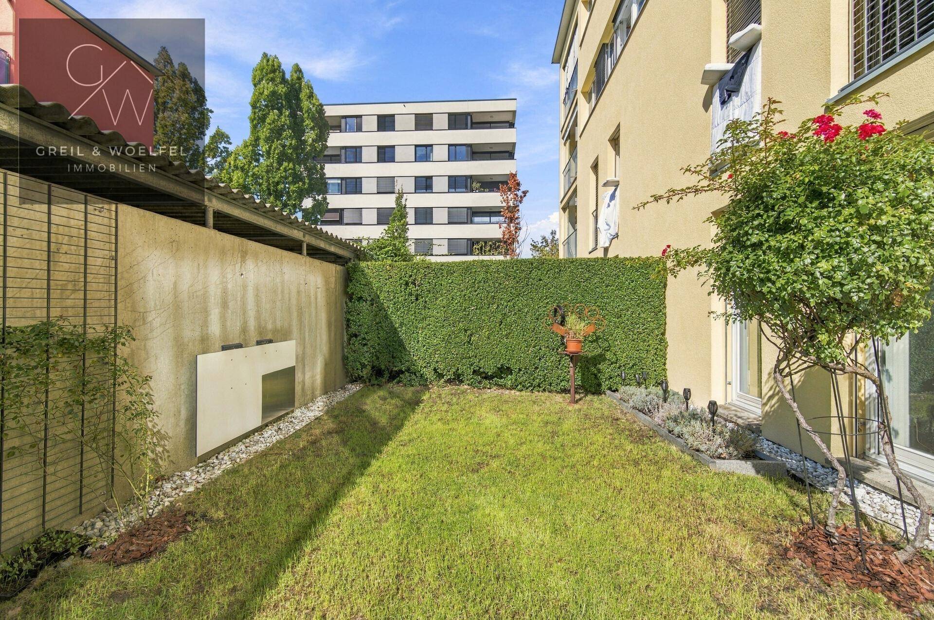 Kleiner, gepflegter Gartenbereich mit Hecke und Blick auf umliegende Wohngebäude.