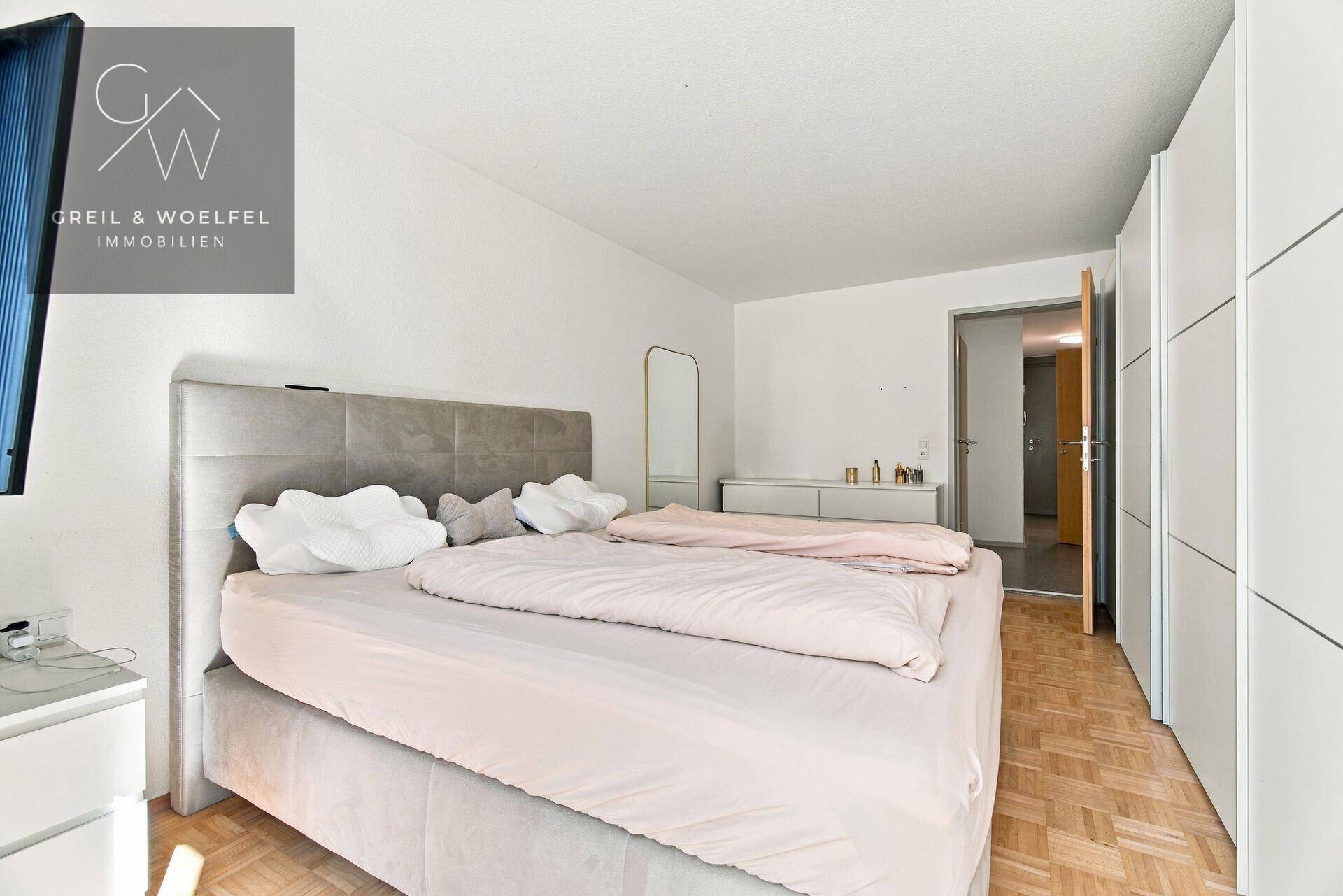 Helles Schlafzimmer mit Parkettboden, großem Bett und integrierten Kleiderschränken.