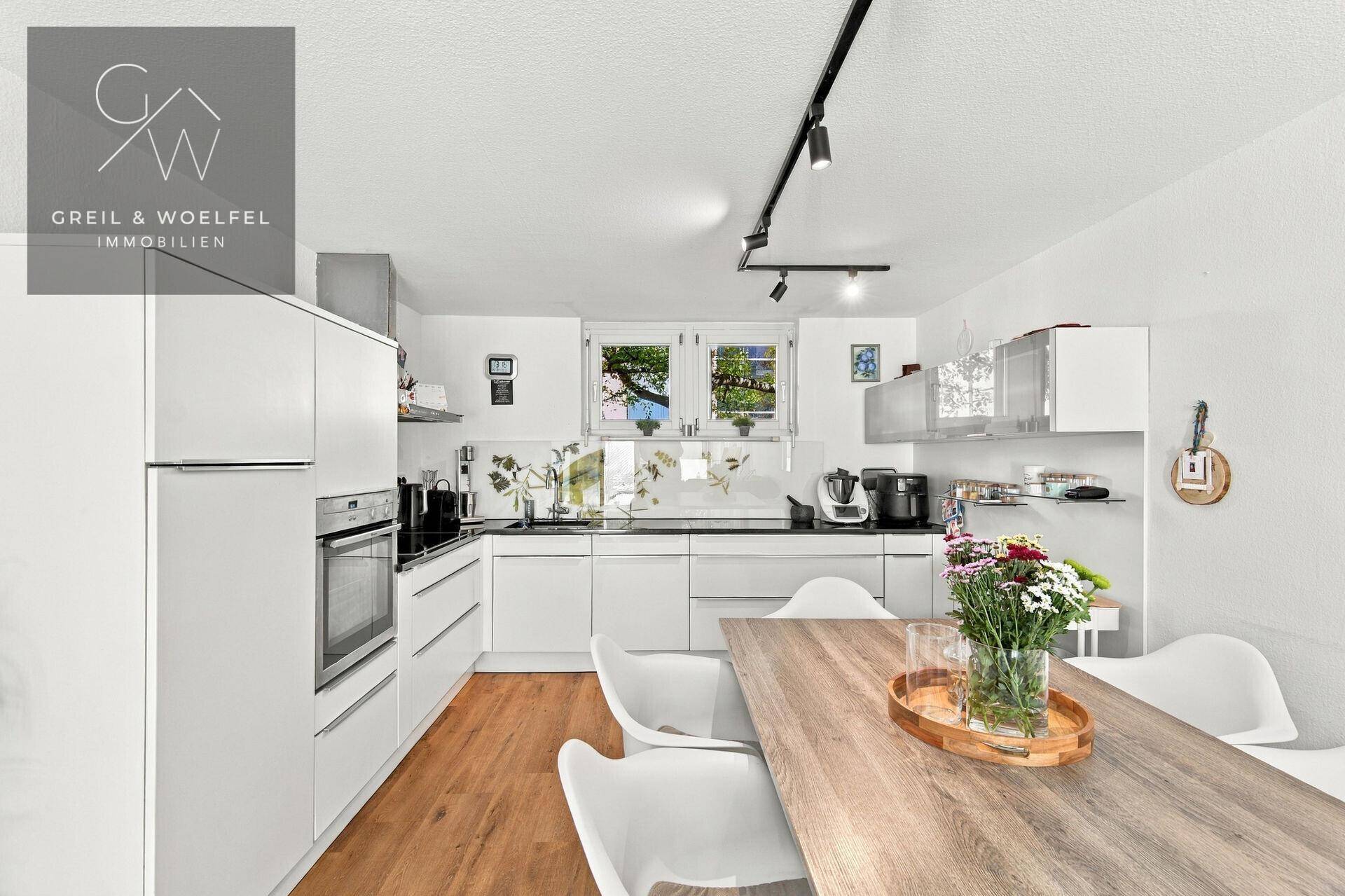 Helle, moderne Küche mit weißen Fronten, Holzboden und Essbereich für gemeinsame Mahlzeiten.