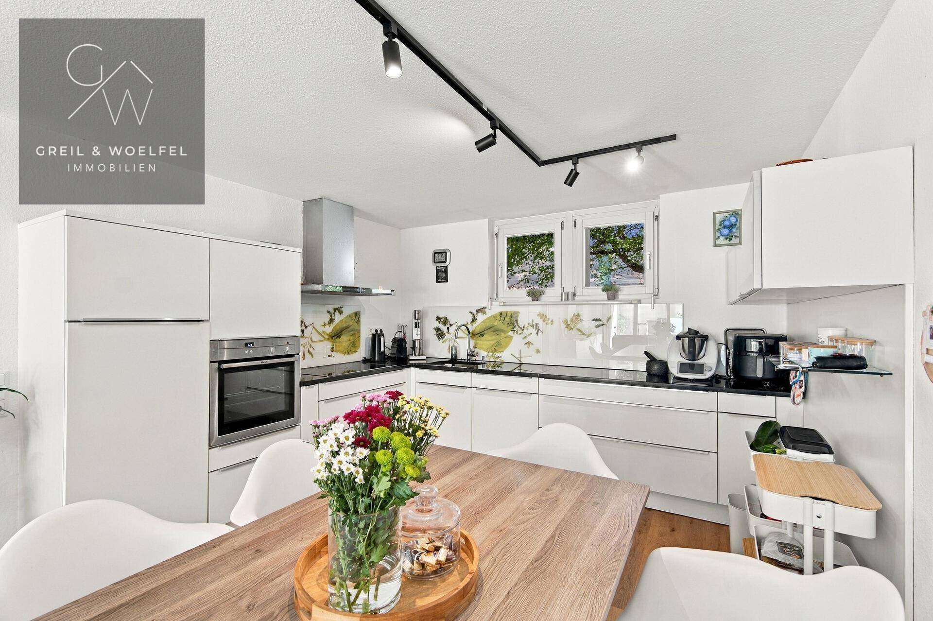 Funktionale Küche mit weißen Schränken, dunkler Arbeitsplatte und Essbereich am Fenster.