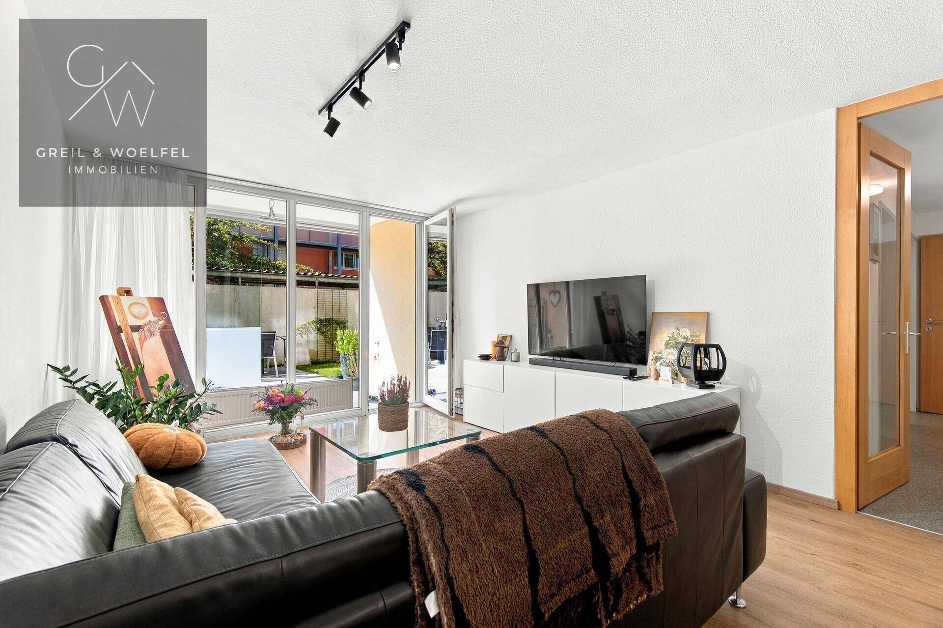 Heller Wohnbereich mit großem Fenster, Sofa und Blick auf den Außenbereich.