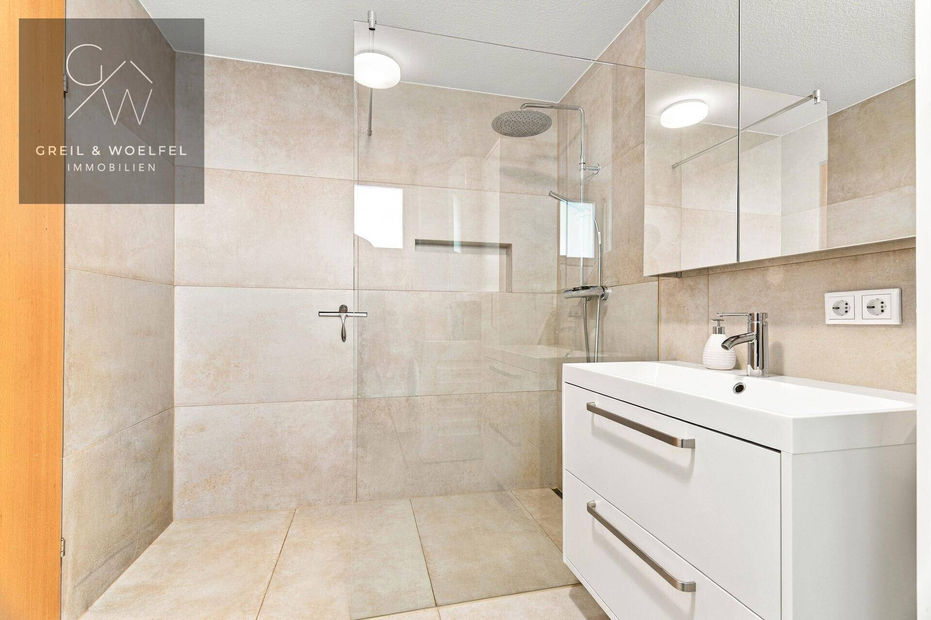 Modernes Badezimmer mit begehbarer Dusche, Regendusche und Waschtisch mit Unterschrank.