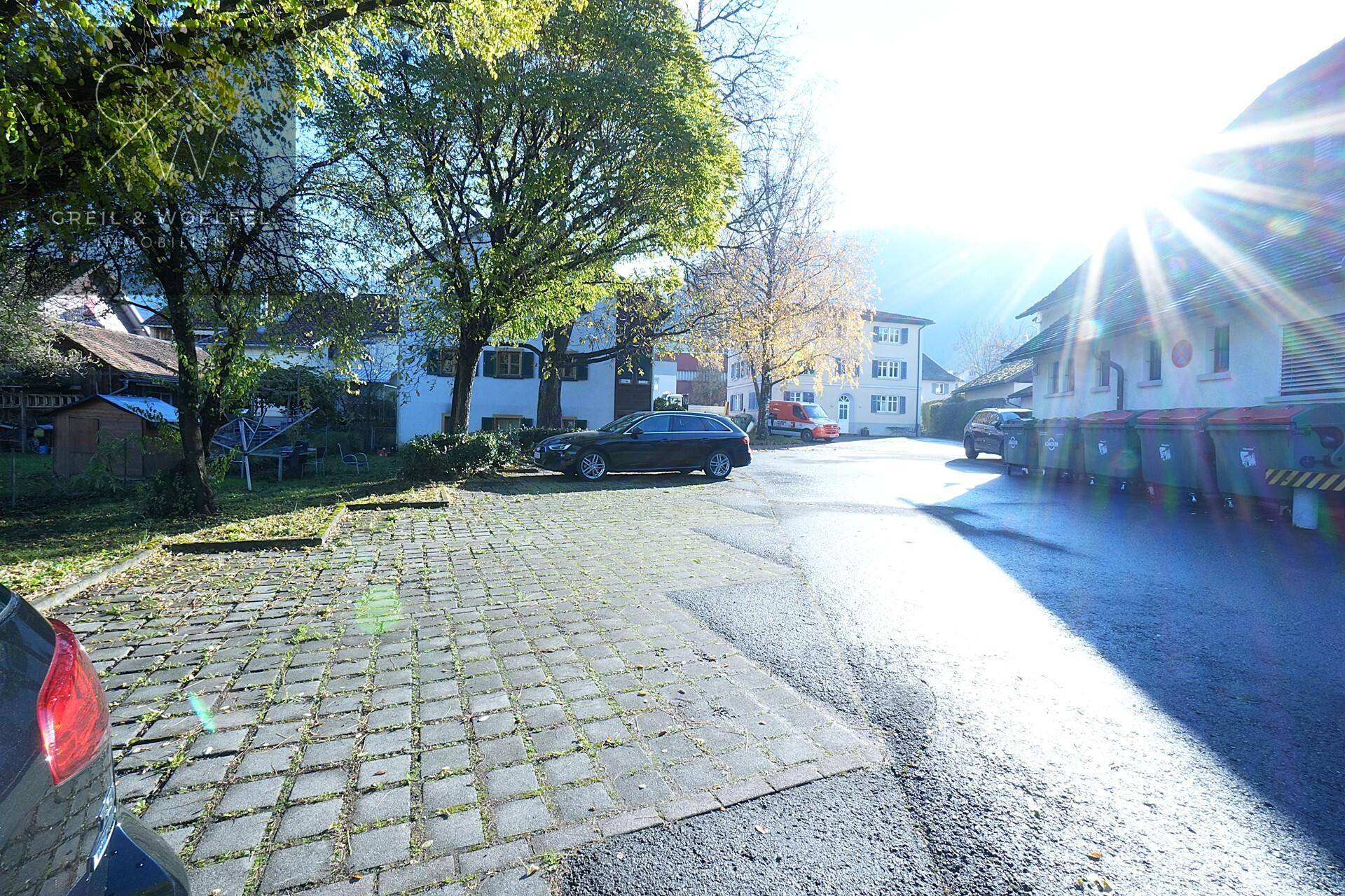 Außenbereich mit gepflasterten Parkplätzen und Gebäuden im Hintergrund an einem sonnigen Tag.