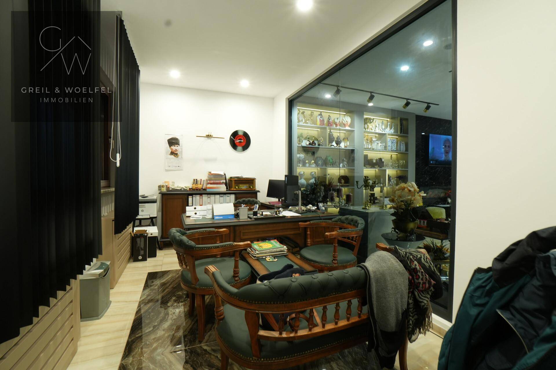 Büro mit klassischem Schreibtisch, bequemen Stühlen und großen Fenstern mit Blick in den Verkaufsraum.