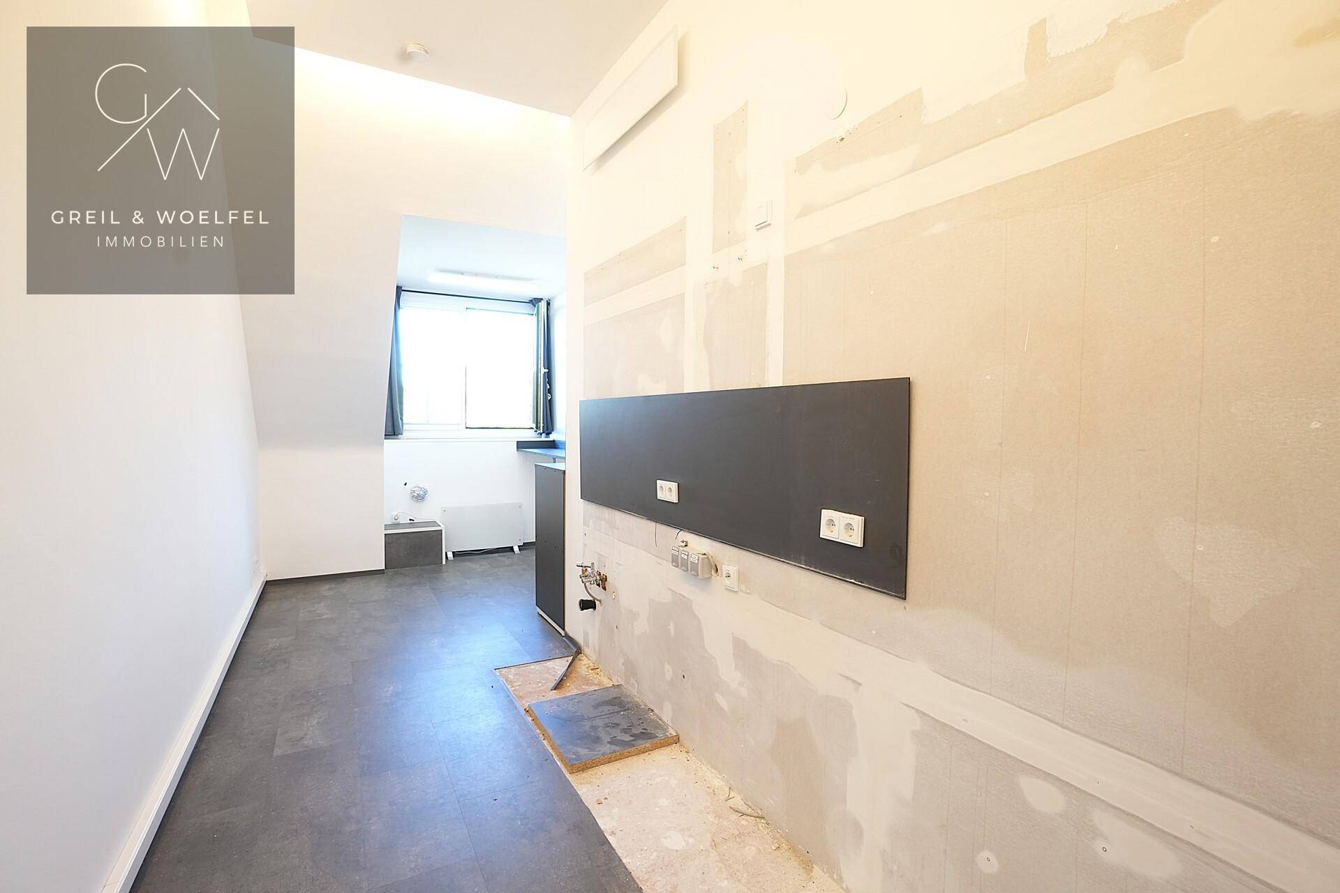 Bereich für eine Teeküche in Renovierung, mit vorbereiteten Anschlüssen und Fenster.