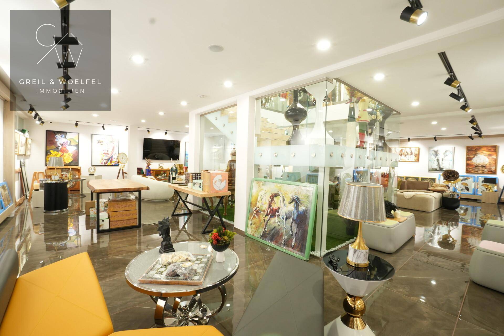 Heller Verkaufsraum mit modernen Möbeln, Kunstwerken und einer transparenten Glaswand.