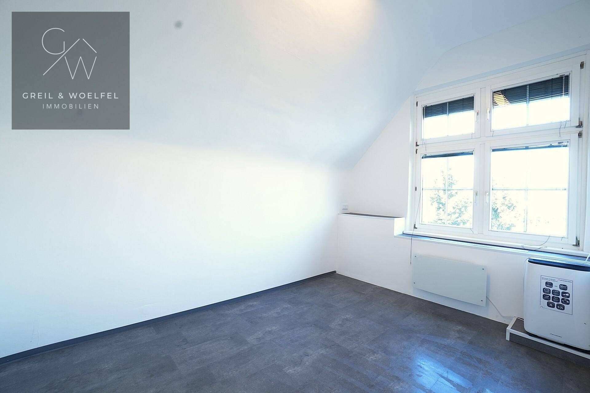 Leerer Büroraum im Dachgeschoss mit Fenster und Heizkörper, bereit zur Nutzung.