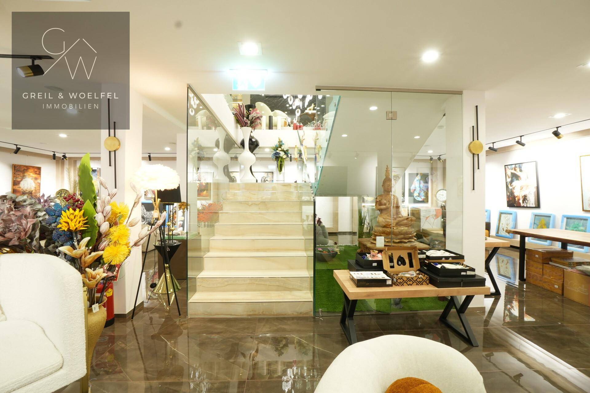 Offener Verkaufsraum mit eleganter Glastreppe, die verschiedene Ebenen verbindet und für Transparenz sorgt.