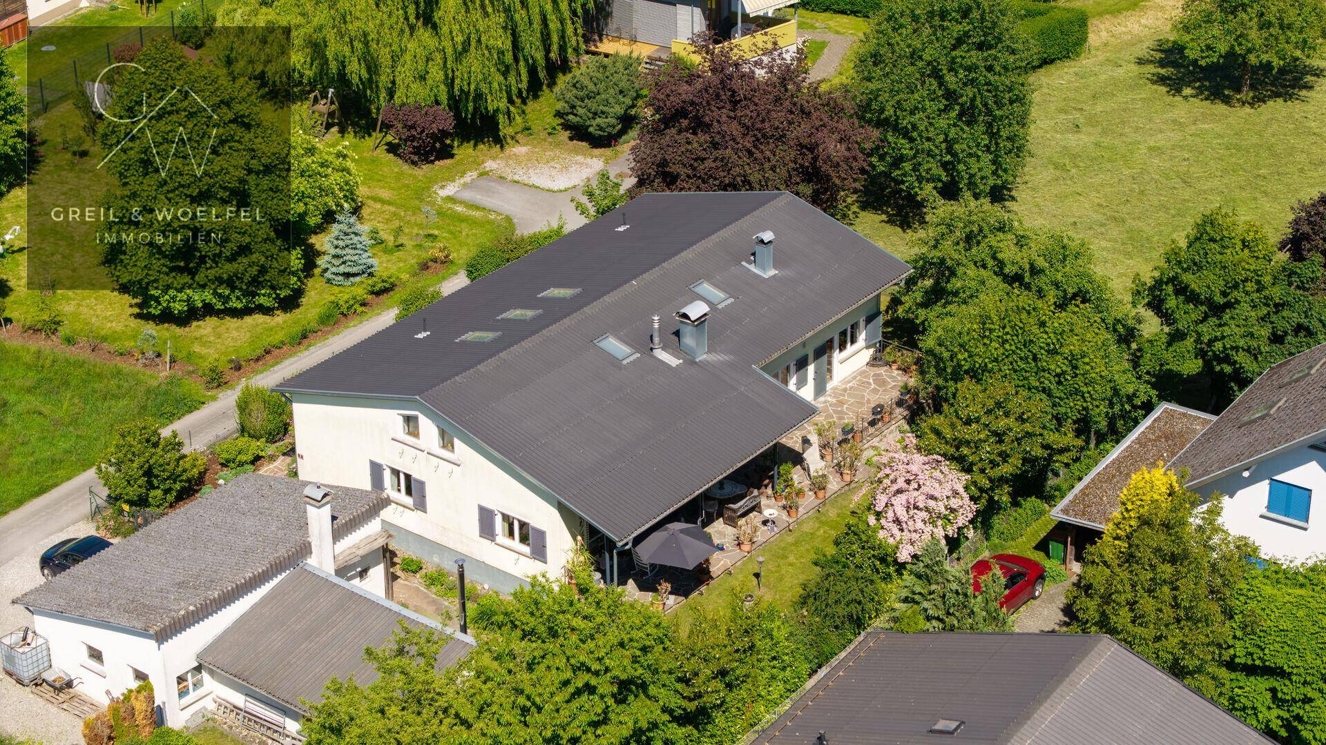 Vogelperspektive des Anwesens mit umliegenden Häusern und viel Grün, unter blauem Himmel.