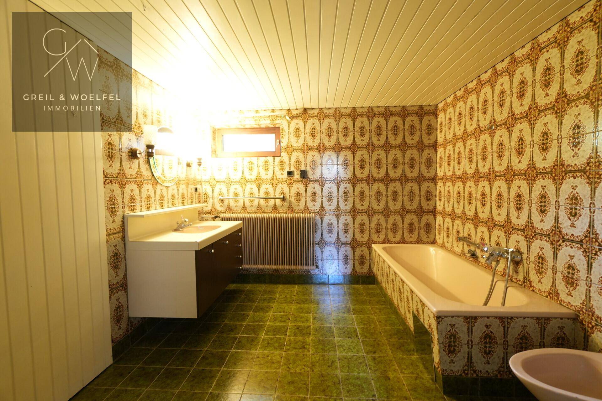 Badezimmer im Vintage-Stil mit gemusterten Fliesen, Badewanne und Fenster, benötigt Modernisierung.
