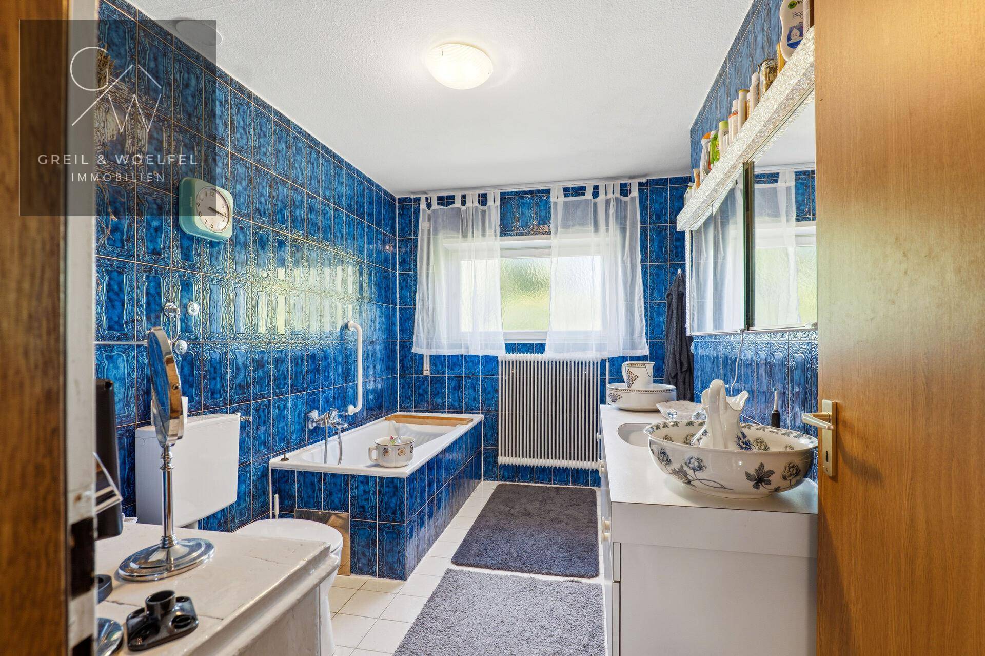 Badezimmer mit blauen Fliesen, Badewanne und Fenster, ausgestattet mit einem einzelnen Waschbecken.