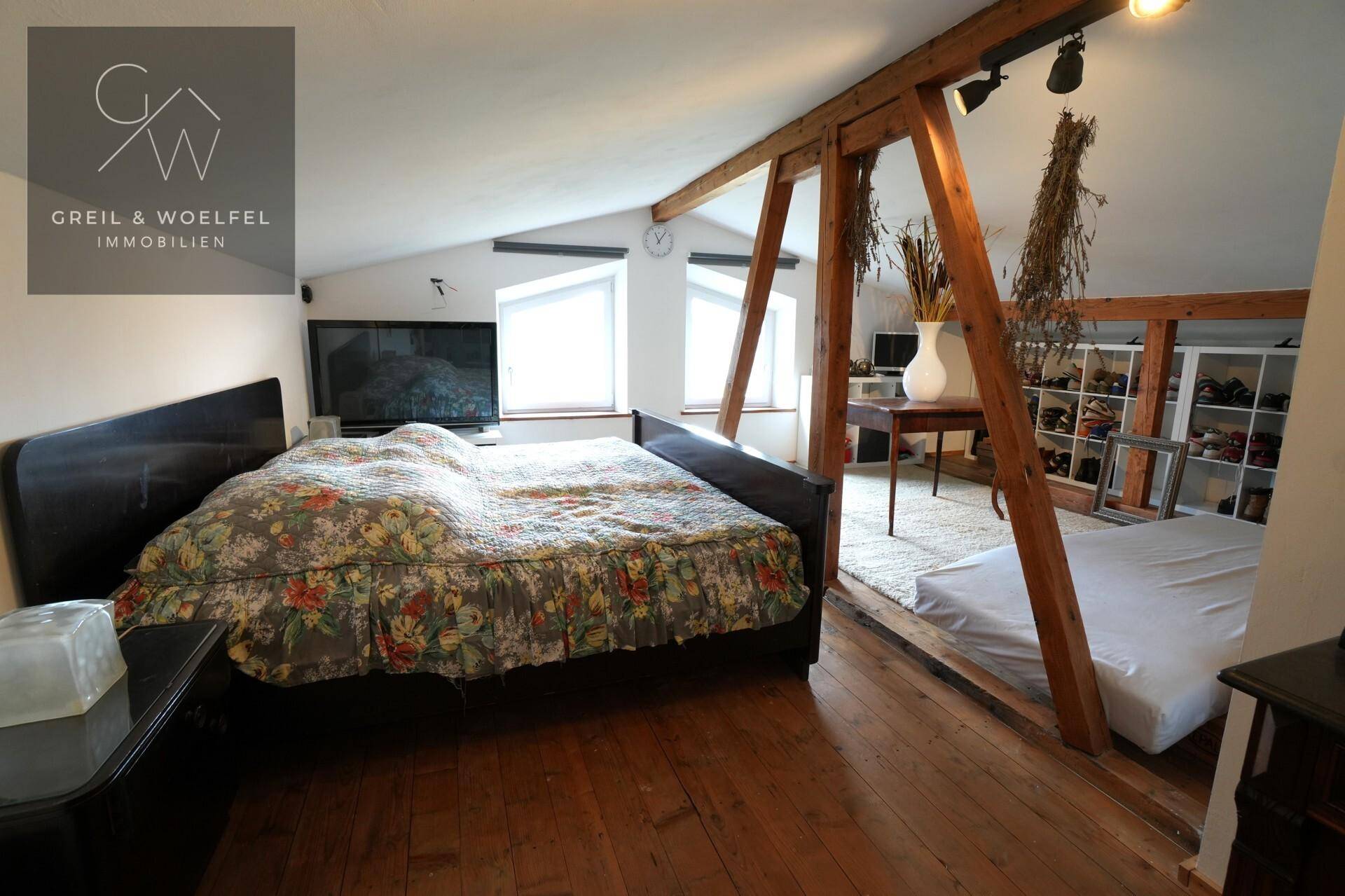 Schlafzimmer im Dachgeschoss mit Holzboden, Dachschrägen und offenem Stauraum, hell und geräumig.