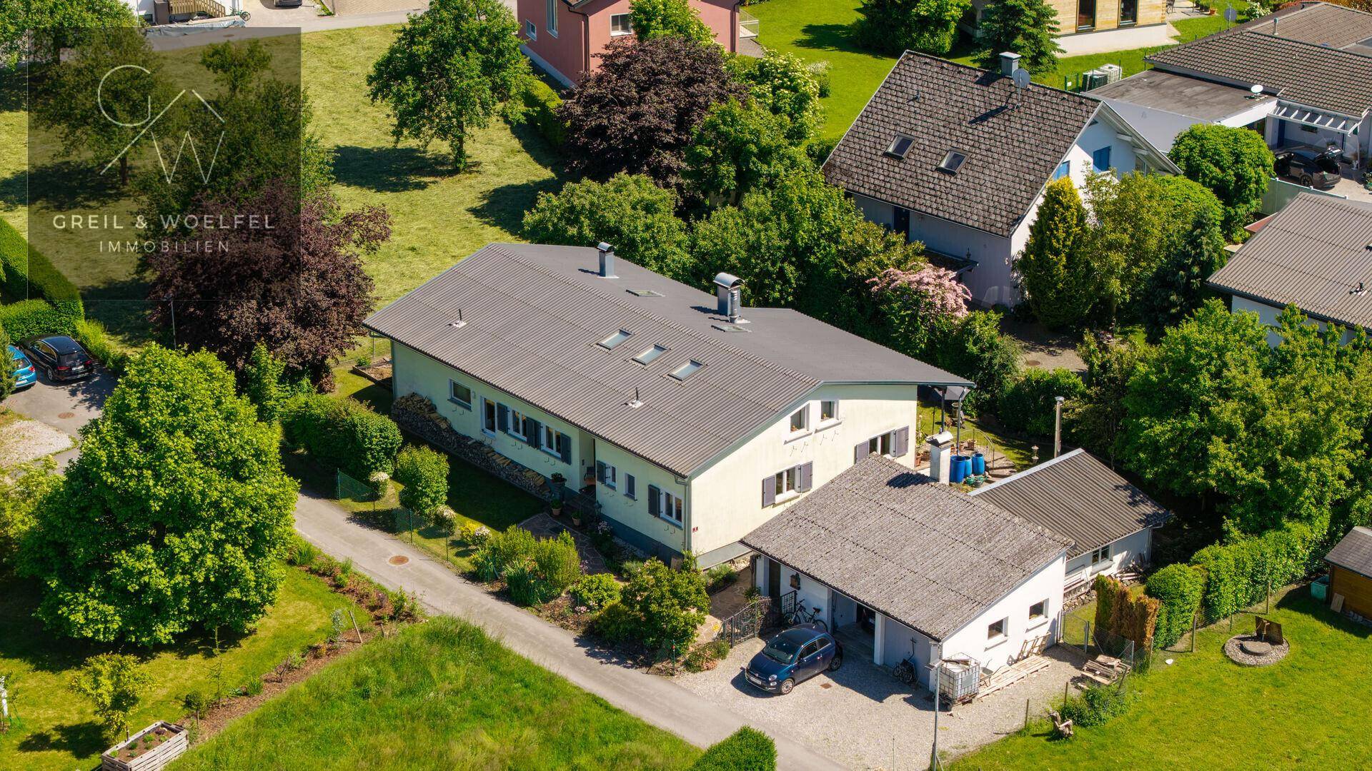 Weitläufige Luftaufnahme des Hauses mit Garage und Zufahrt, eingebettet in grüne Umgebung.