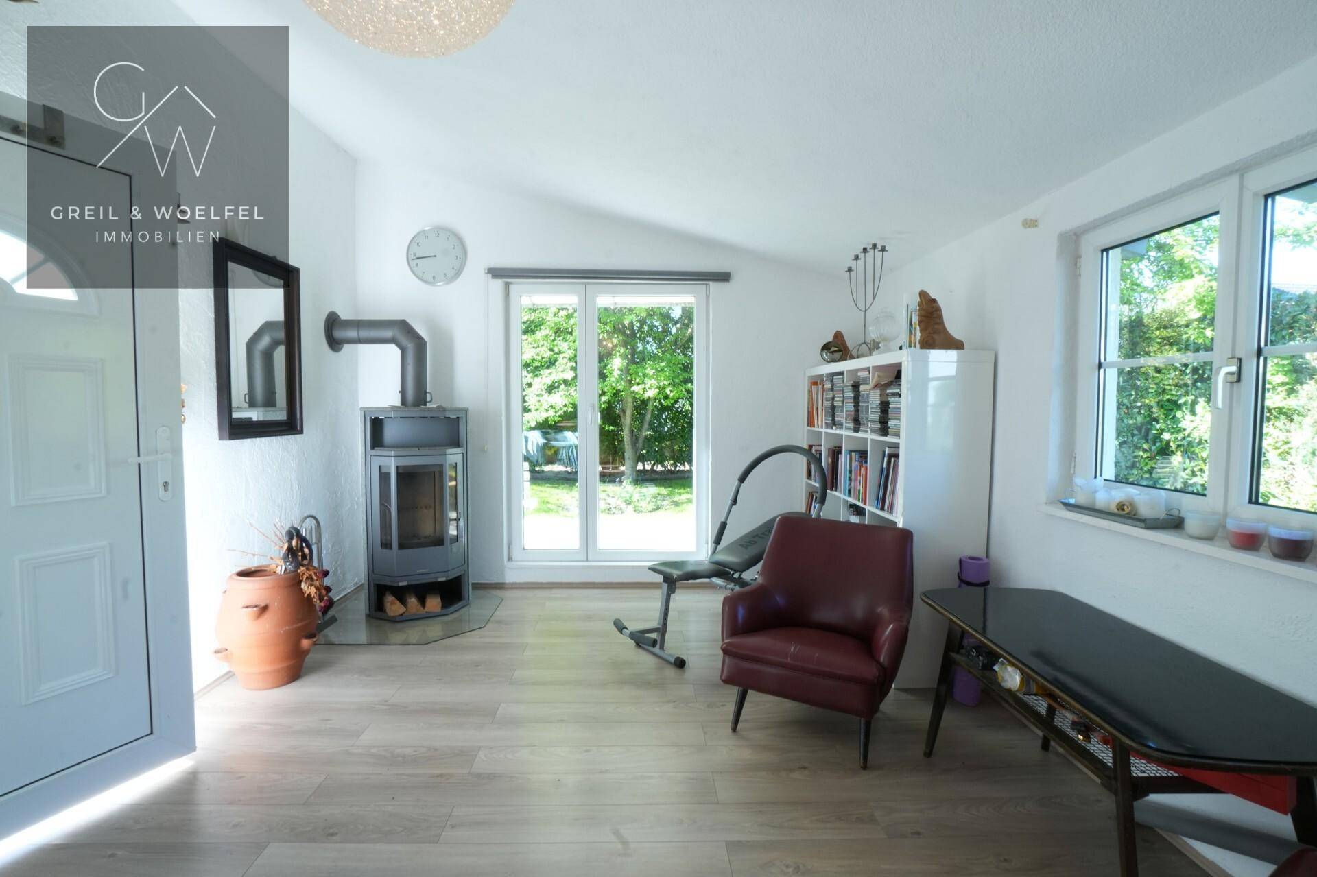 Helles Wohnzimmer mit Kaminofen, Laminatboden und großen Fenstern mit Blick in den Garten.