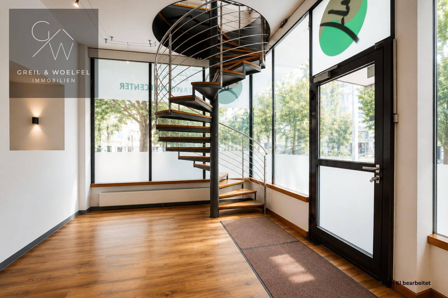 Heller Eingangsbereich mit eleganter Wendeltreppe, großen Fenstern und Holzfußboden.
