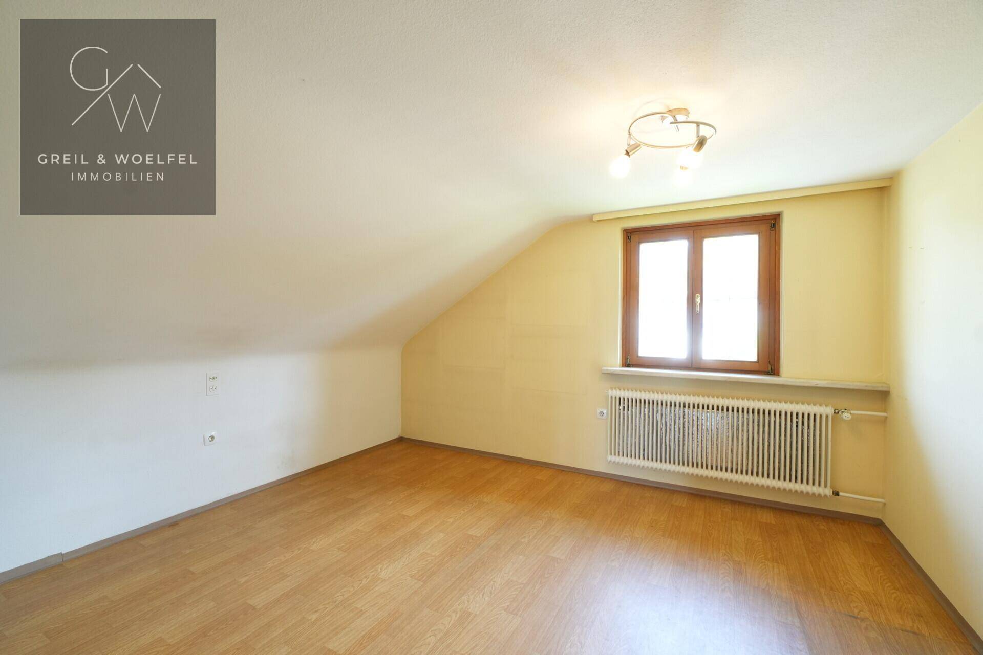 Dachgeschosszimmer mit schrägen Wänden, Laminatboden und Fenster, hell und geräumig.