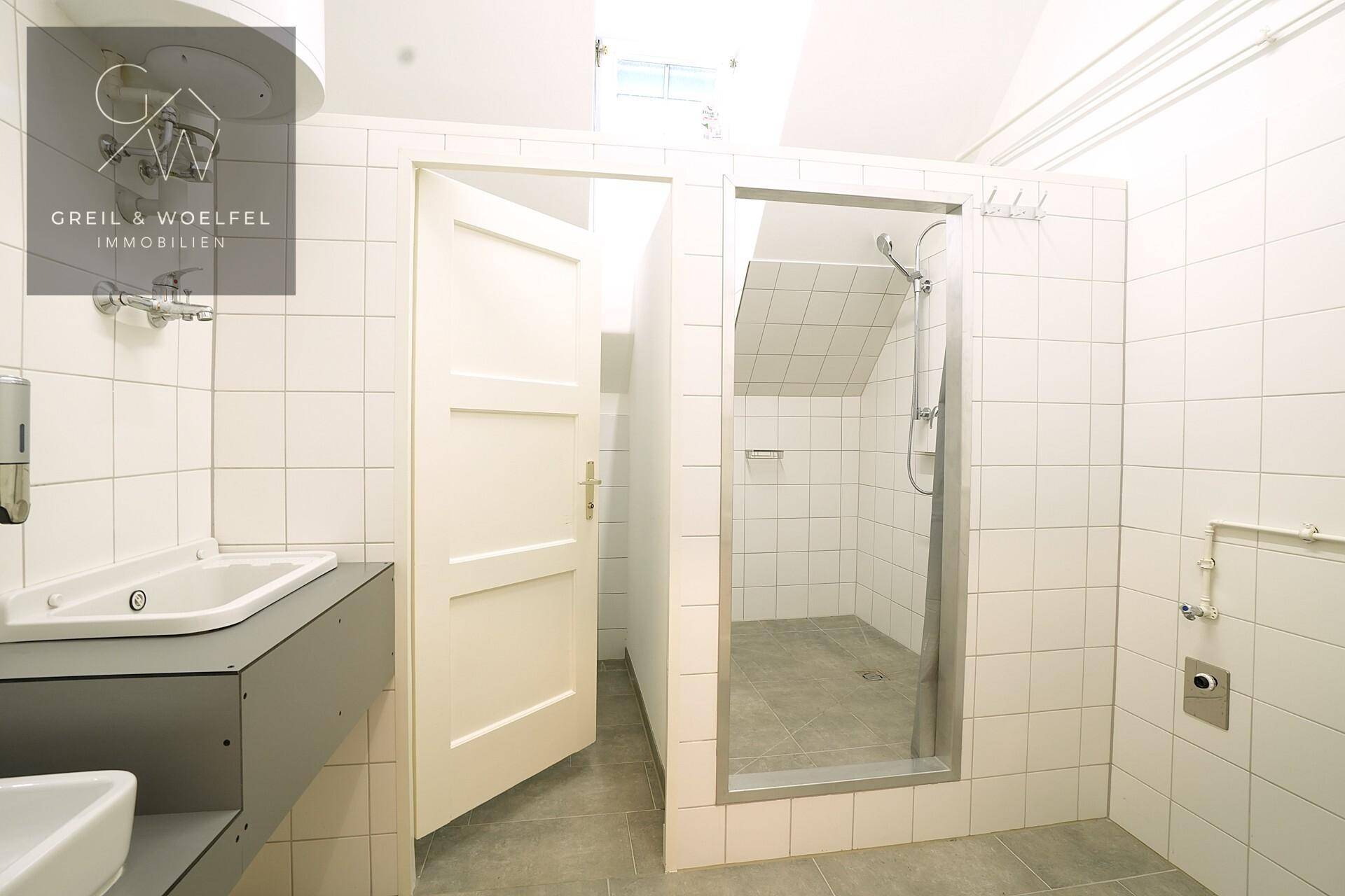 Badezimmer mit weißen Fliesen, Duschkabine und Waschbecken, in gutem Zustand.