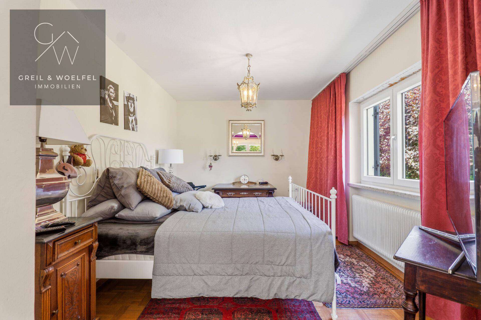 Gemütliches Schlafzimmer mit Doppelbett, Holzmöbeln und roten Vorhängen, hell durch Fenster.