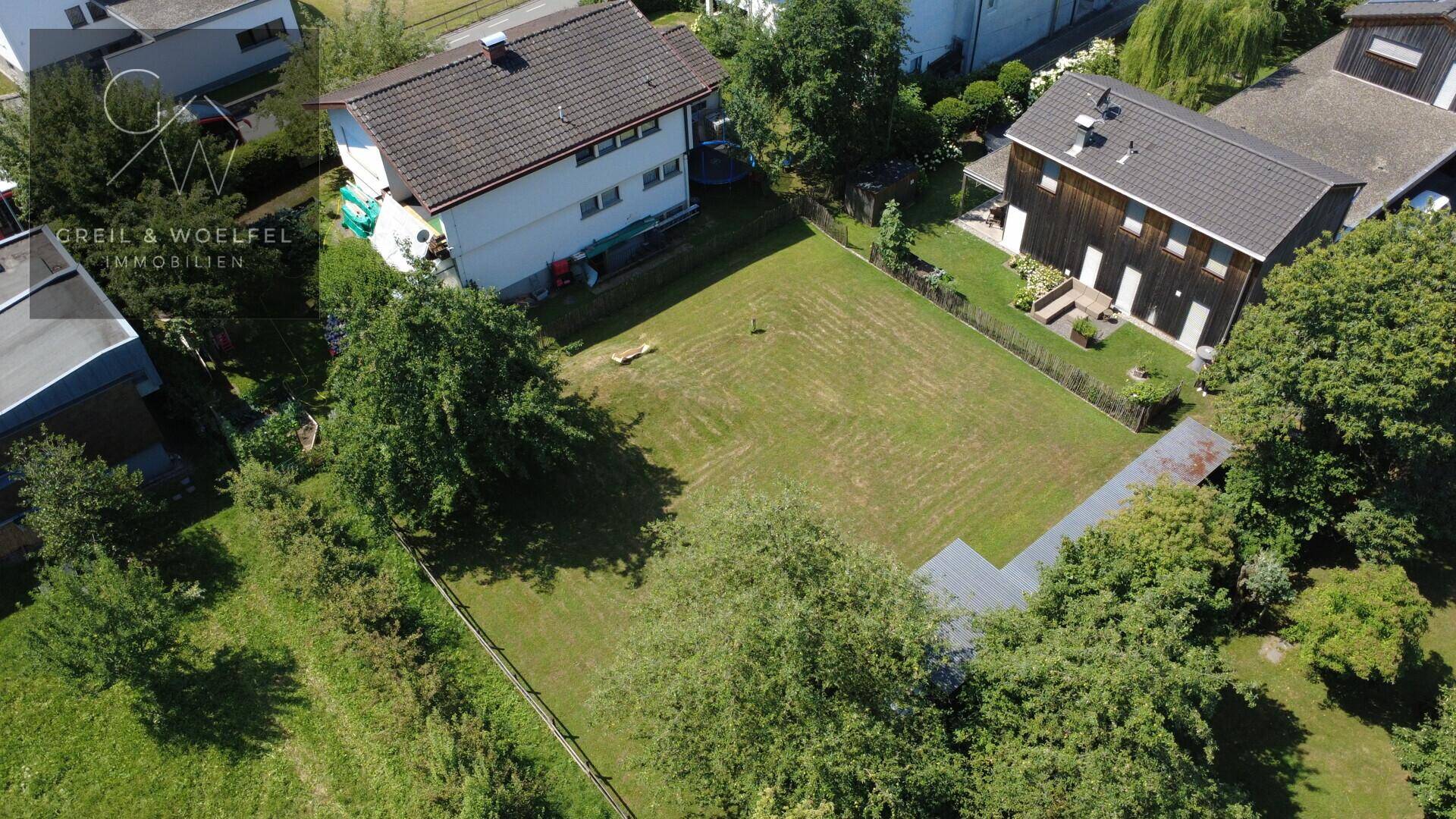 Luftaufnahme eines Hauses mit großem Rasengarten, umgeben von weiteren Wohnhäusern und viel Grün.
