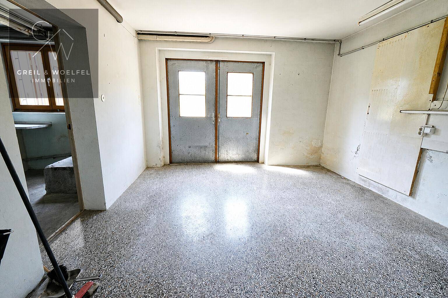 Geräumige Garage mit Betonboden und Doppeltüren, bietet Platz für Fahrzeuge und Lagerung.